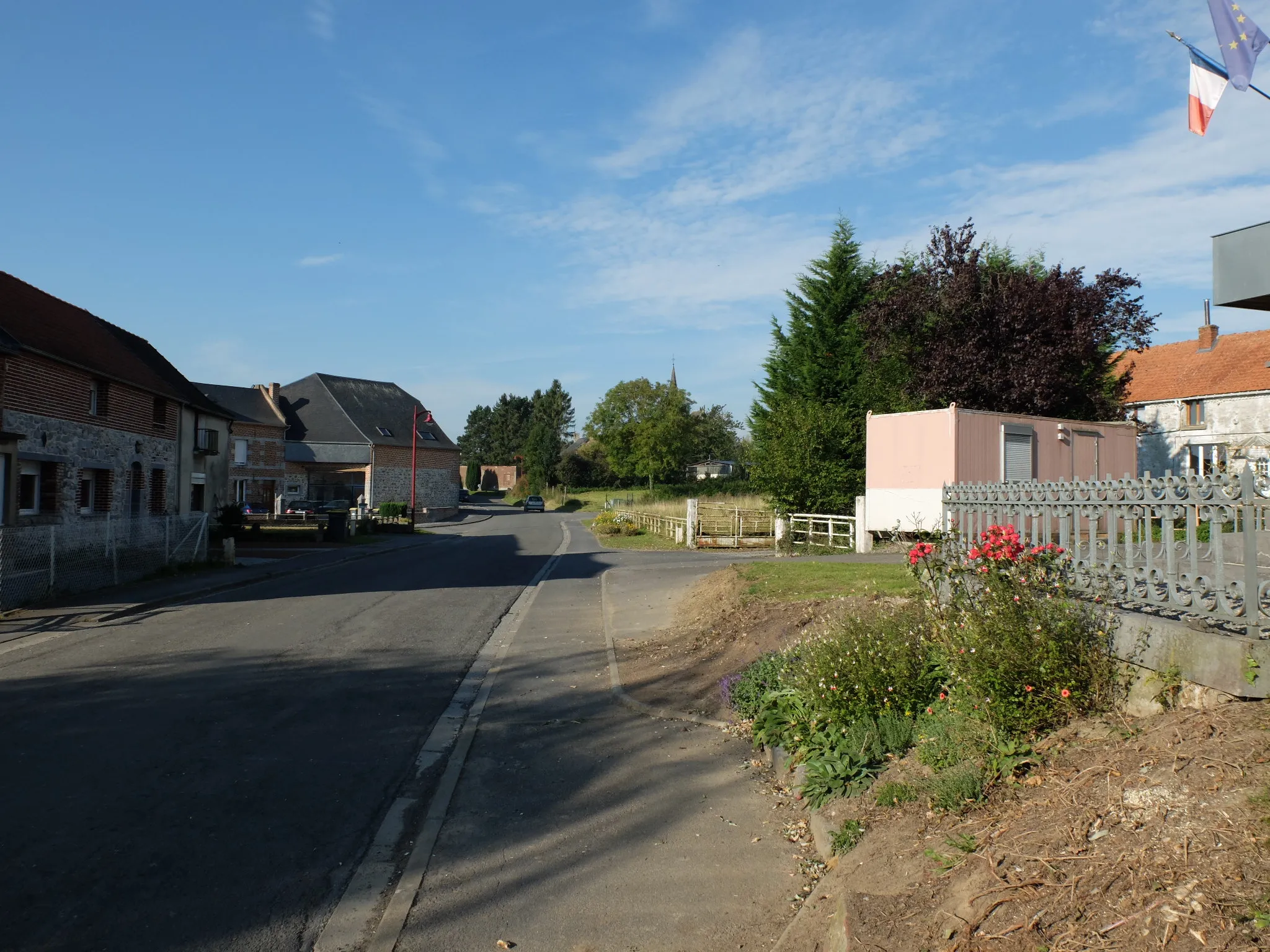 Photo showing: Vue de la Grand Rue de Sassegnies à côté du monument aux morts. Au fond, le clocher de l'église est visible.