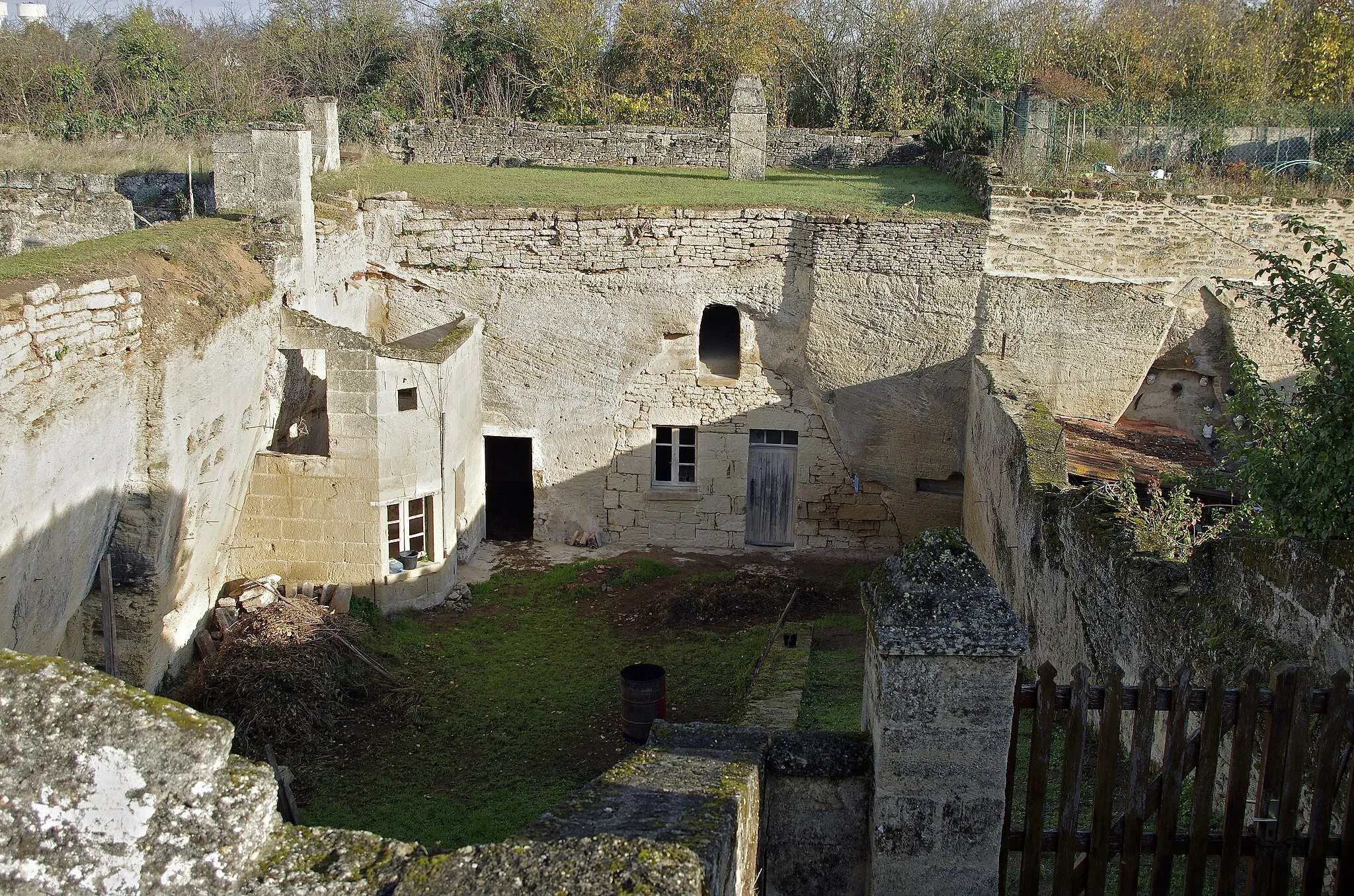 Photo showing: Doué-la-Fontaine (Maine-et-Loire)
Habitation troglodyte rue des Perrières.
Il y a 10 millions d'années, le quart nord-ouest de la France, excepté la Bretagne, est recouvert par ce que les géologues appellent la Mer des Faluns. Des sédiments marins se déposent. Les dépôts, mêlant sable et débris de coquilles, peuvent atteindre une vingtaine de mètres d'épaisseur dans des cuvettes litorales comme celle de Doué-la-Fontaine.
Facile à creuser et à travailler, le calcaire des faluns a des caractéristiques le font utiliser pour différents usages, telle la pierre de taille, les moellons, le sable ou comme matière première pour la fabrication de la chaux. On l’utilise également pour l’amendement des terres siliceuses et acides.
Jusqu'à la fin du XIXe siècle, les paysans ont creusé le sol pour en extraire le "falun" utilisé pour fertiliser les champs. Les caves qui ont été aménagées abritaient, à la fin du XVIIIe siècle près de la moitié de la population du sud-saumurois.
Fin XVIIIe siècle et début XIXe, Doué connait l'apparition de grandes carrières est consécutive à un développement important des activité de construction. A cette époque apparaissent de nouveaux habitats souterrains, ceux des carriers, comme aux Perrières.
D'autres cavités sont plus anciennes, comme une ancienne carrière mérovingienne du Ve siècle ou l'on fabriquait les sarcophages. Les premiers habitats souterrains fortifiés apparaissent au IXe siècle. Des habitants de Saumur se seraient réfugiés dans ces cavernes pour échapper aux raids des vikings au IXe siècle.
www.les-perrieres.com/fr/les-perrieres/user/documents/201...

www.lauragais-patrimoine.fr/BIBLIOTHEQUE/SURVIVANCE-L.GRA...