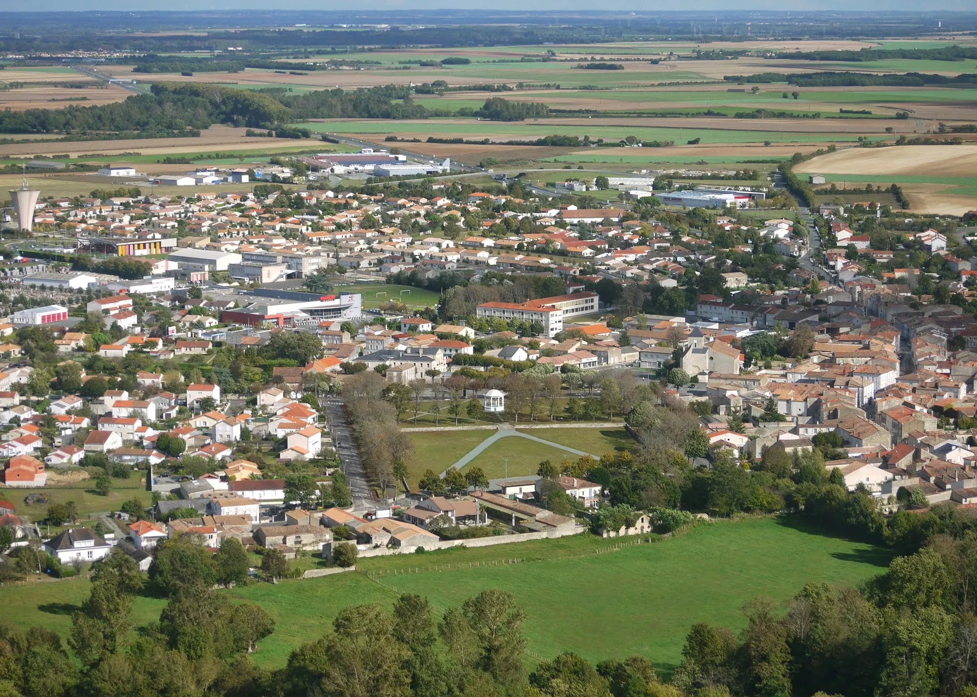 Photo showing: Vue aérienne de Mauzé sur le Mignon avec le champ de foire et le kiosque à musique au premier plan.