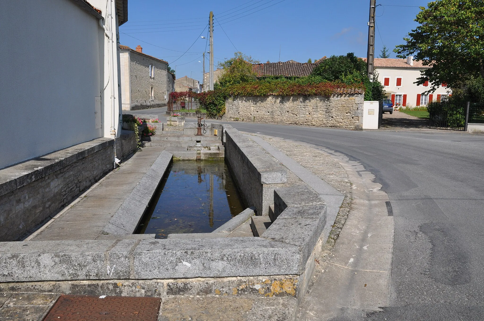 Photo showing: Ce lavoir, qui a été réduit pour élargir la route à l'occasion des Grands Travaux de 1994, est assis sur une source où, autrefois, et grâce à une pompe à bras toujours présente, chacun pouvait se servir en eau potable.