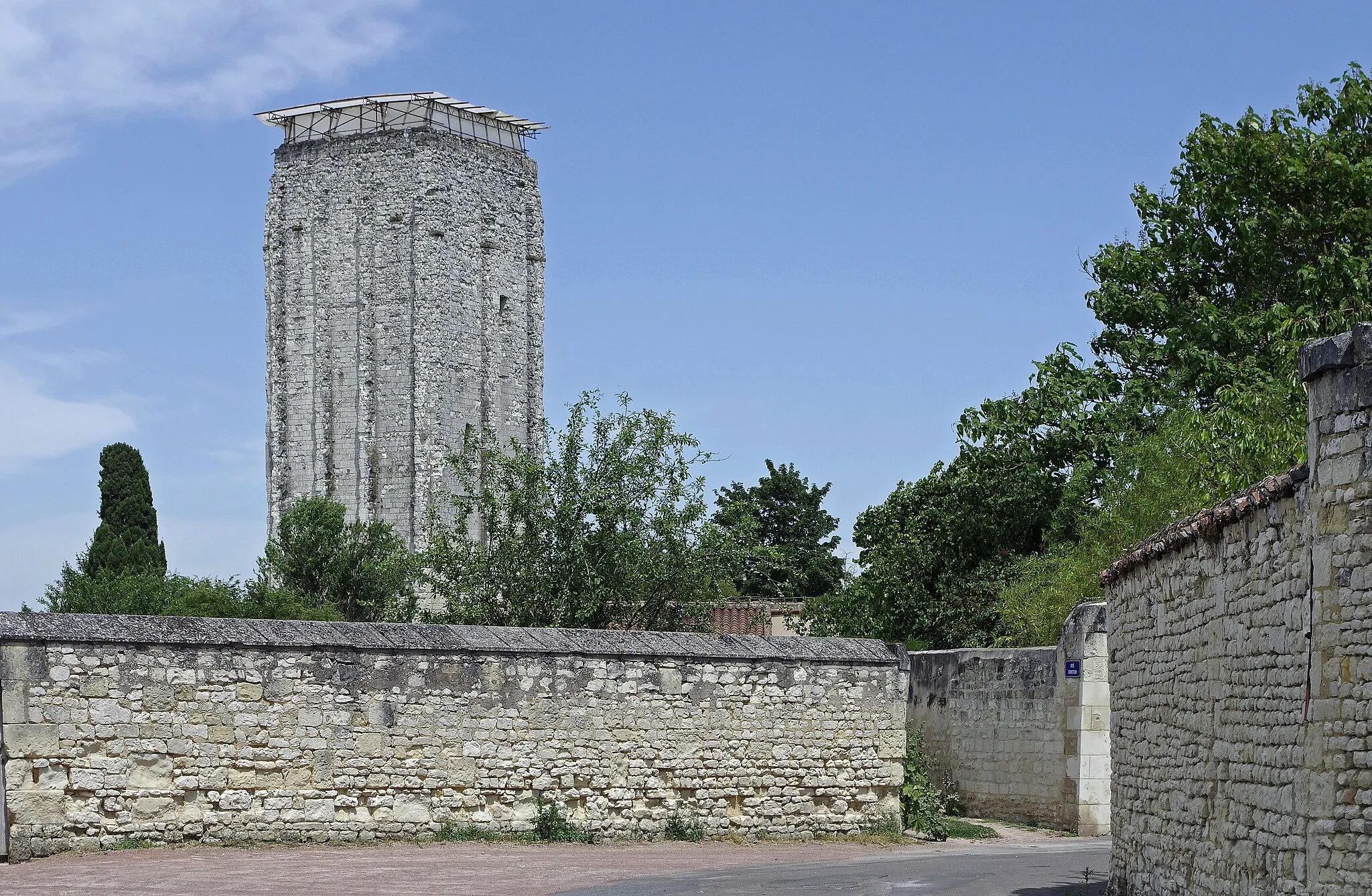 Photo showing: Loudun (Vienne)
Le Donjon ou Tour Carrée.
La tour, de 31 m de haut, servait de tour de guet. L'absence de puits et de latrines, nécessaires pour soutenir un siège, semble bien indiquer qu'elle n'a jamais eu un caractère défensif d'un véritable donjon. Elle comportait trois étages séparés par des planchers.

La Tour Carrée, fut probablement construite d'abord en bois, vers 1040 par Foulques Nerra, Comte d’Anjou et Seigneur de Loudun.
Au XIIe siècle, elle fut rasée et rebâtie dans sa forme actuelle, sur les mêmes fondations, par le petit fils de Foulques Nerra, Foulques le Rechin.
Philippe Auguste investira la place en 1206, et va fortifier la ville en l'entourant d'une enceinte avec une quinzine de tours. Il construira également un donjon doont il ne reste que les fondations.
En 1214 : Jean-sans-Terre achète l’aide des barons poitevins : les Chauvigny, les Mauléons, les Thouars. Il s'allie également à l'empereur d'Allemagne et au comte de Flandre, contre le roi de France. Jean-sans-Terre occupe Angers. Mais il est battu à La Roche-aux-Moines et ses alliés (L'empereur Otton IV de Brunswick et Ferrand de Flandre) le sont à Bouvines le 27 juillet 1214. Le 18 septembre 1214, Philippe Auguste impose la paix de Chinon à Jean-sans-Terre.  Le roi d’Angleterre garde l'Aquitaine, mais paye 60 000 livres au roi de France et renonce à l’Anjou, au Maine, à la Touraine, au Poitou.
Au printemps 1360, le traité de Brétigny met fin à plus de 20 ans de combats. Le traité de paix qui suit (à Calais) est calamiteux pour les Valois. Édouard III renonçe au titre de roi de France mais il obtient la souveraineté sur la Guyenne, la Saintonge, l’Agenais, le Limousin, le Périgord, le Quercy et l’Angoumois. 
Le poitou retourne sous la coupe Anglaise. Le royaume de France retourne 150 ans en arrière.
Le fils de Jean II le Bon, Charles V, se lance dans une guerre de reconquète du Poitou. Les barons poitevins ont massivement choisi le parti anglais, mais du Guesclin reprend une série de places fortes aux anglais (Montcontour, Poitiers, La Rochelle...). A l'hiver 1372, le traité de Loudun mettra fin à cette reconquète: les seigneurs poitevins prêtent serment au roi de France. Mais auparavant, Loudun avait été cédée par Charles V au duc d'Anjou en 1367, en échange de Champtoceaux.
Les ducs d'Anjou feront construire une demeure appelée le Palais Royal de Sicile, dont malheureusement il ne reste rien. La tour a été enclavée dans les bâtiments du Palais Royal.
René d"Anjou devra céder Loudun à Louis XI qui fera de la ville un baillage. Par la suite, Loudun dépendra de Saumur.
Au milieu du XVIème siècle, le roi de Navarre, Henri, qui deviendra Henri IV, prend la ville. La religion Protestante a de nombreux adeptes à Loudun.  Après la bataille de Montcontour et le siège de Poitiers, le futur Henri III  reprendra Loudun et fera détruire l'ancienne forteresse de Philippe Auguste.  La ville passera donc alternativement du Parti Catholique au Parti Protestant. L'Edit de Nantes (1598) fait de Loudun une des places de sureté protestantes.
Au XVIIème siècle, à la demande de Richelieu, les places fortes protestantes furent démolies. Loudun comprenait alors un grand nombre de protestants, le château sera démoli en 1633. Lors de la démolition du château, la tour fut cependant épargnée, sur demande du secrétaire de Louis XIII, Lucas, ce pourquoi on lui donne parfois le nom de Tour "Lucas". L'année d'avant, en 1632, en été, une épidémie de Peste emportait plusieurs milliers de Loudanais.
Au XVIIIe, un violent tremblement de terre touchera le reste des murailles et l'église.
Loudun accueillera favorablement la Révolution.

Au pied de la Tour Carrée, on peut visiter un jardin d'inspiration médiévale, comptant entre autres les plantes ayant servi à l'élaboration du polychreston, médicament élaboré au XVIIe par Théophraste Renaudot.