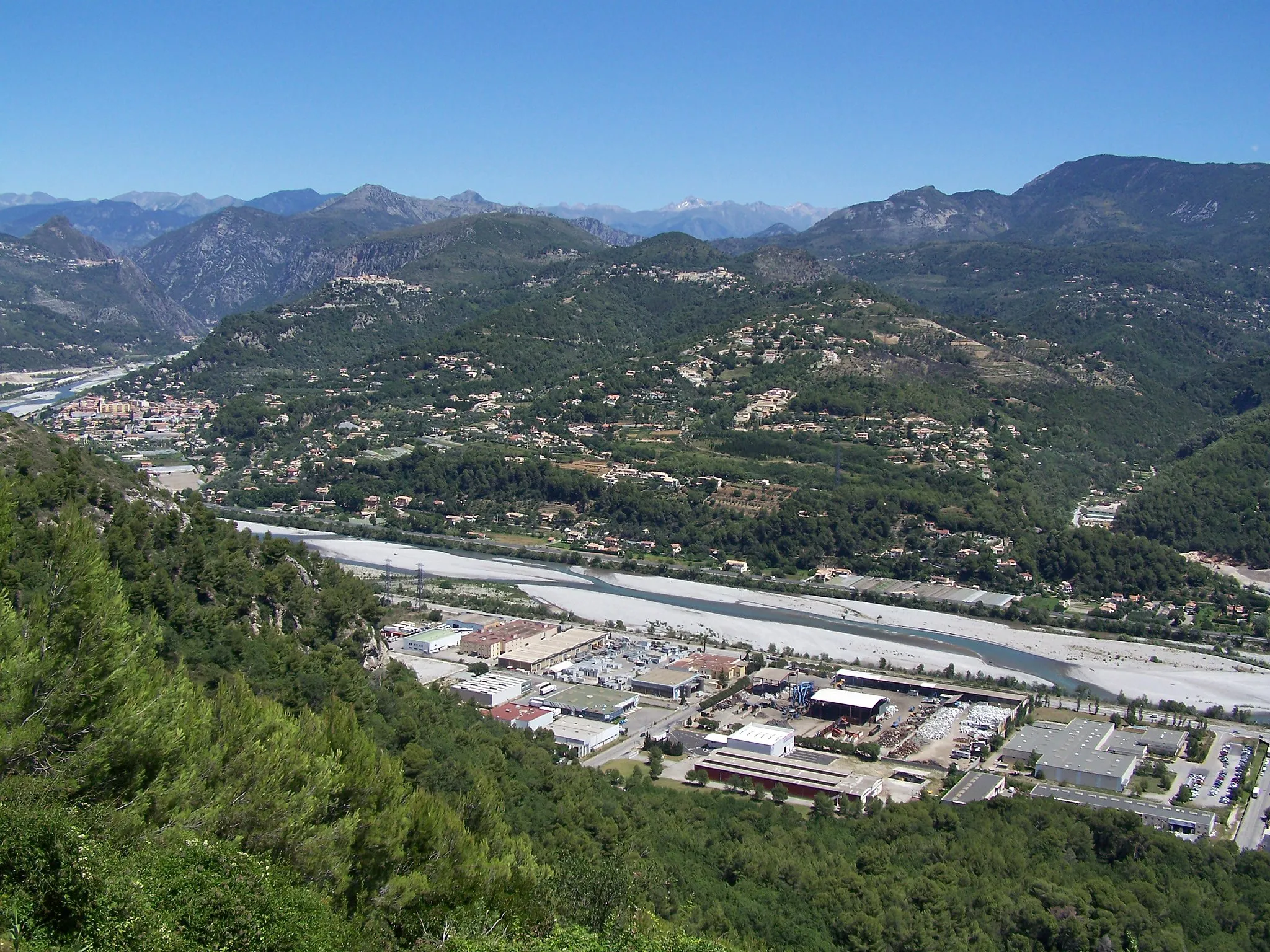 Photo showing: La partie finale de la vallée du fleuve Var (Alpes-maritimes, France) juste après son confluent avec les rivières Vésubie et Estéron. Sur cette photographie prise du belvédère de Carros, on peut voir en bas et au milieu la zone industrielle de Carros, en haut et à droite la chaîne du Férion (1412m) et en arrière-plan les sommets frontaliers entre la France et l'Italie (avec de la neige résiduelle sur le Gelas, point culminant du département à 3143m).