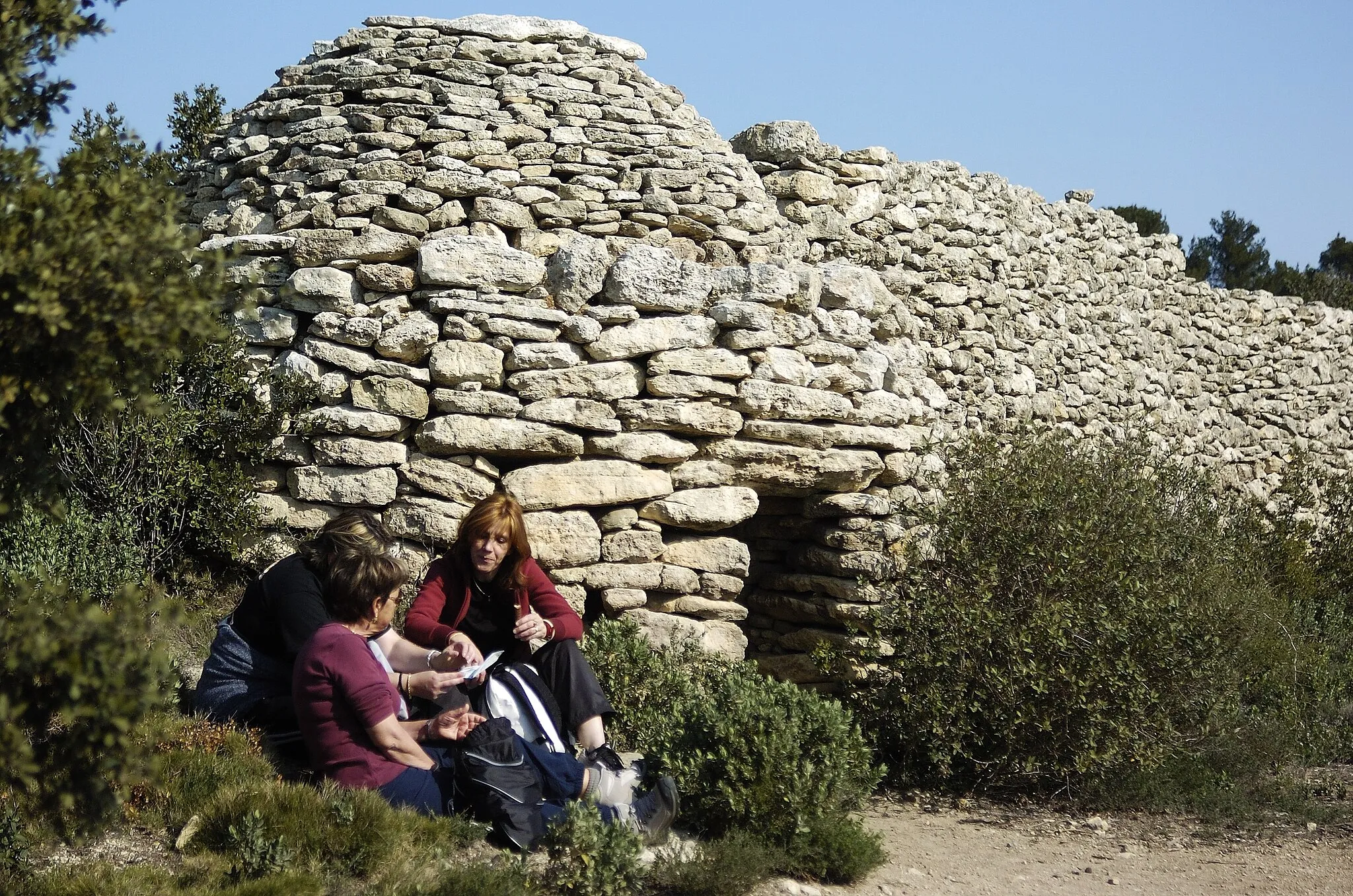 Photo showing: Val de Cuech Ouest, Salon-de-Provence, Bouches-du-Rhône: at one end of a dry stone wall, an agricultural stone hut with circular plan and recessed cupola-like roof.