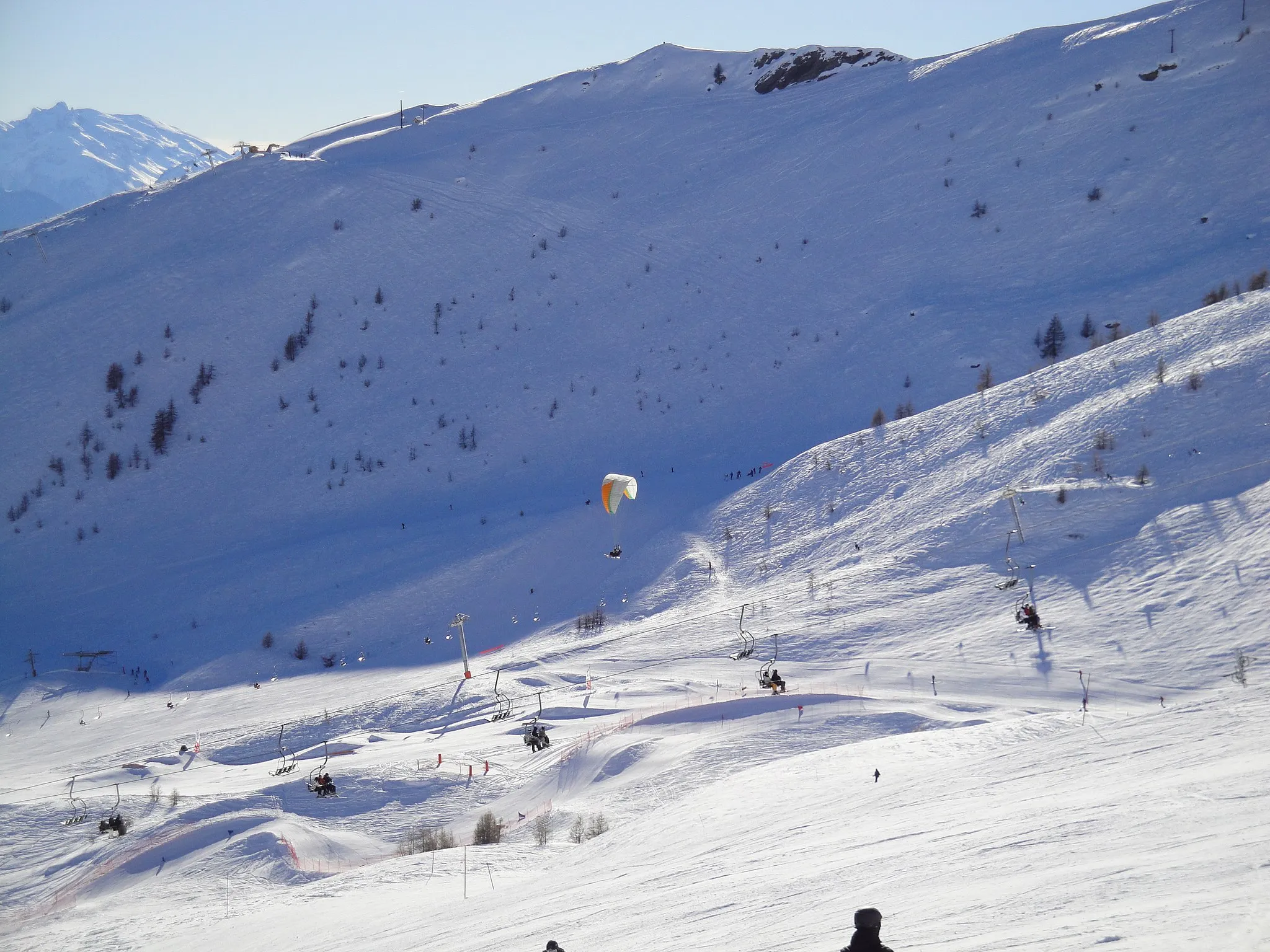 Photo showing: Un parapente survole les pistes de Puy Saint Vincent. On distingue au fond du vallon la piste de boarder-cross.