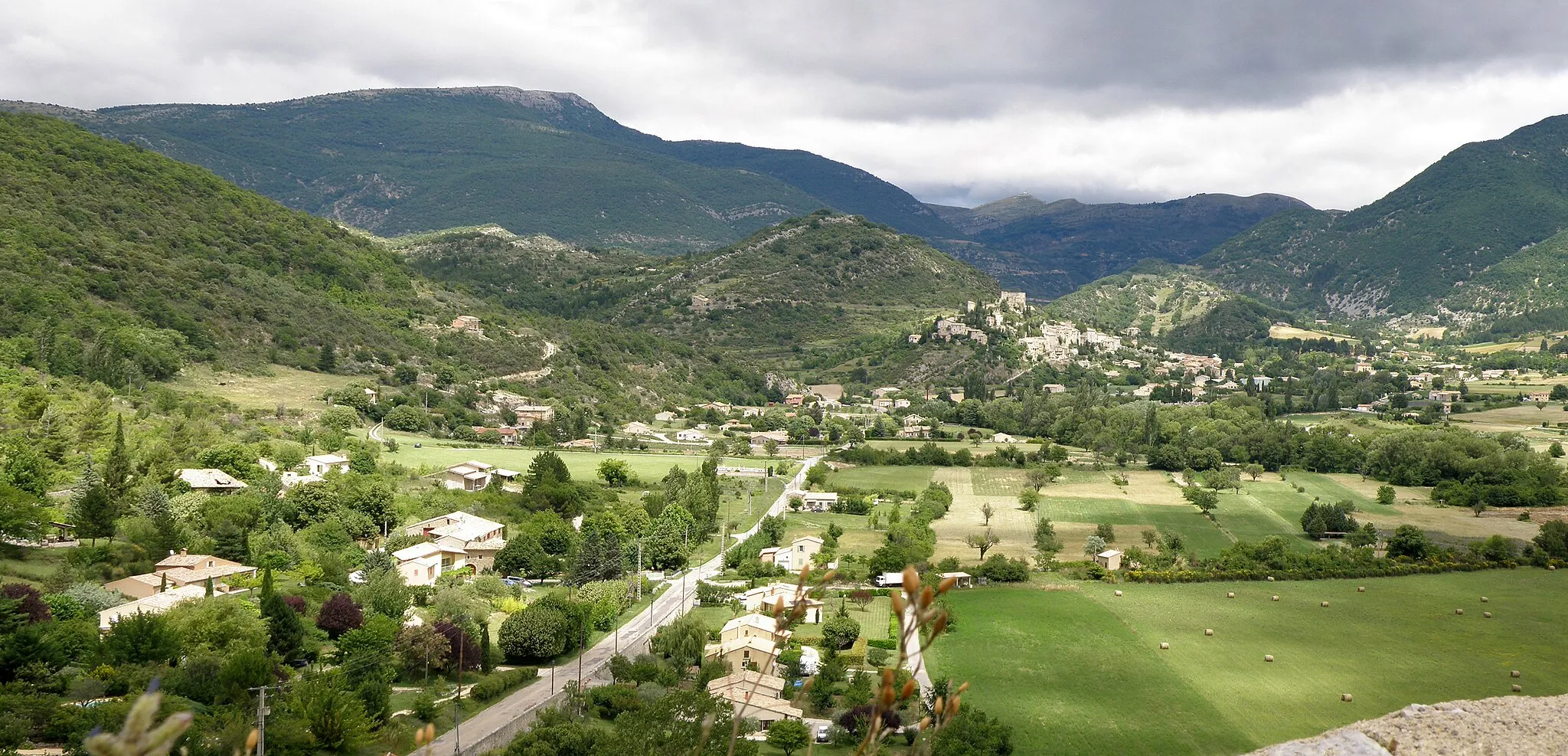 Photo showing: Plaine de Reilhanette / Montbrun-les-Bains (Drôme, France), vue depuis l'esplanade du château de Reilhanette. Nous regardons vers l'est-nord-est. Dans le lointain, le bourg perché de Montbrun-les-Bains avec son château ruiné. La route au centre gauche est la départementale D159a.