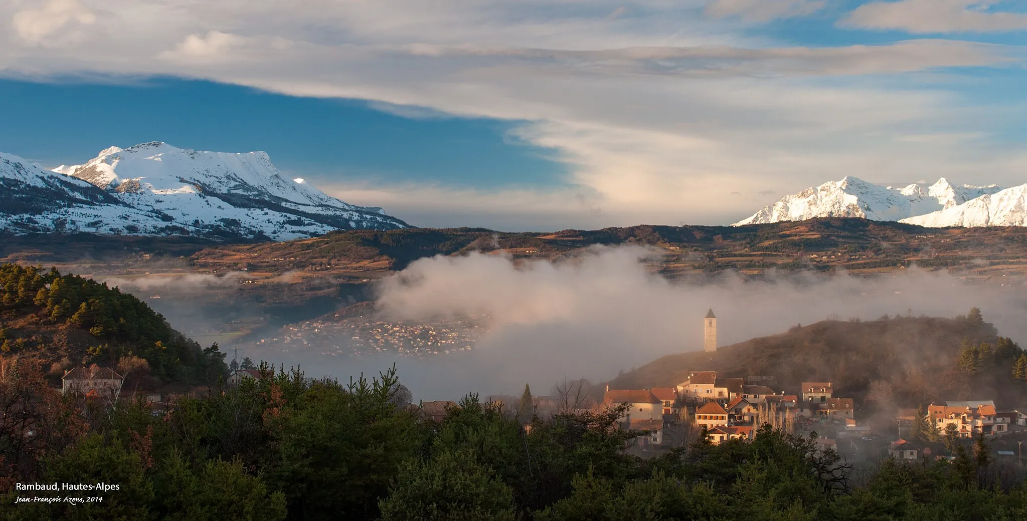 Photo showing: Le village de Rambaud (Hautes-Alpes) vu depuis les hauteurs en hiver, avec sa tour caractéristique ; une partie de la ville de Gap visible à l’arrière-plan