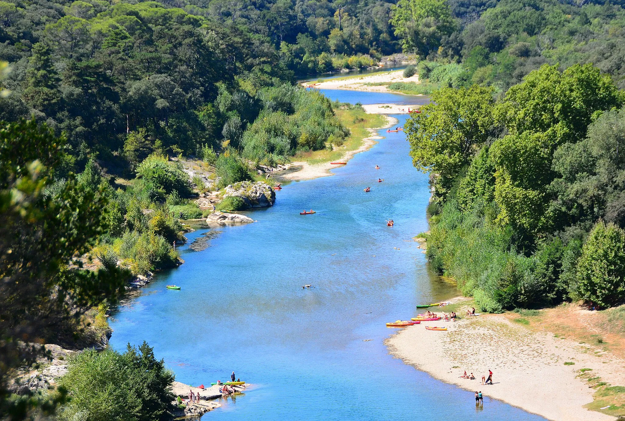 Photo showing: The River Gard or Gardon in southern France flows from  the Cévennes mountain range and ends where it joins the Rhône River at Comps, north of Beaucaire.
It's very popular with locals and visitors and provides plenty opportunities for having fun on or in the water which can be quite warm in summer.

The photo was taken from high above on the amazing 2000 year old Roman Pont du Garde.