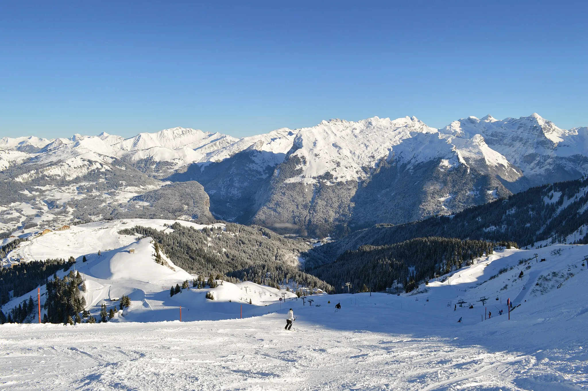 Photo showing: A winter's view from below the Tête des Saix, at the intersection of the Marmotte and Perce-neige slopes, towards Samoëns 1600 (located far left), Samoëns Village (located center, hidden in the valley), and the mountains beyond.
