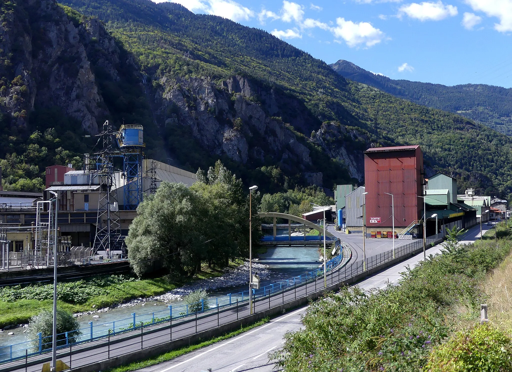 Photo showing: Sight, from Tarentaise railway line, of Carbone Savoie industrial plant crossed by Isère river, in Notre-Dame-de-Briançon, Savoie, France.