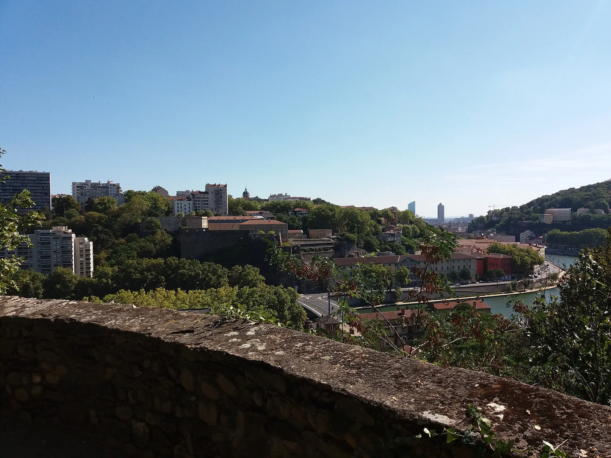 Photo showing: Vue sur Lyon et la Saône (principalement la rive gauche, côté nord), depuis le fort de Vaise (avec un bout de muret) en rive gauche (côté sud).
Pont Kœnig sur la Saône.
En face du pont, le fort Saint-Jean.
A gauche du fort, le premier immeuble du quai Joseph Gillet.
A droite du fort, le Grenier d'abondance.

A droite du Grenier d'abondance, dans le début du tournant de la Saône, le bâtiment rouge de l'ancien hôtel de la Butte donnant sur les hauts arbres de la place de la Butte, au pied de la montée de la Butte.