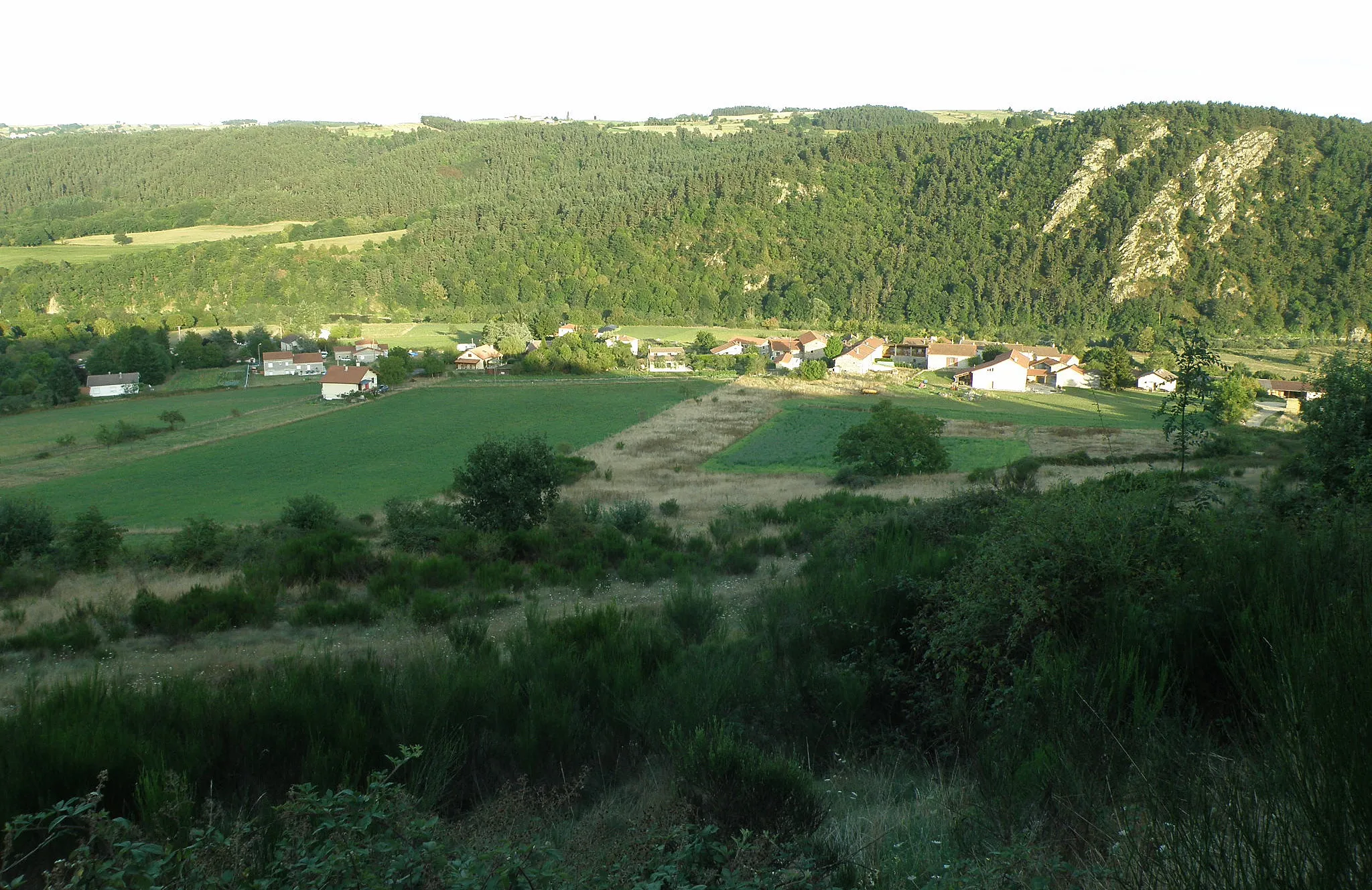 Photo showing: Beauzac, dép. de la Haute-Loire, France (Auvergne). Hameau de Brenas, dans le sud de la commune. Photo prise depuis le chemin qui, escaladant les Côtes du Suc, va au hameau de la Para. Les falaises à l'arrière-plan à droite sont les Rochers de Peyre. Sur la ligne de crête au centre gauche: hameau du Fraisse (comm. de Beauzac). La Loire, dont on aperçoit un peu les eaux à gauche, coule de droite à gauche au pied des falaises. (Coup d'oeil vers le sud-est.)