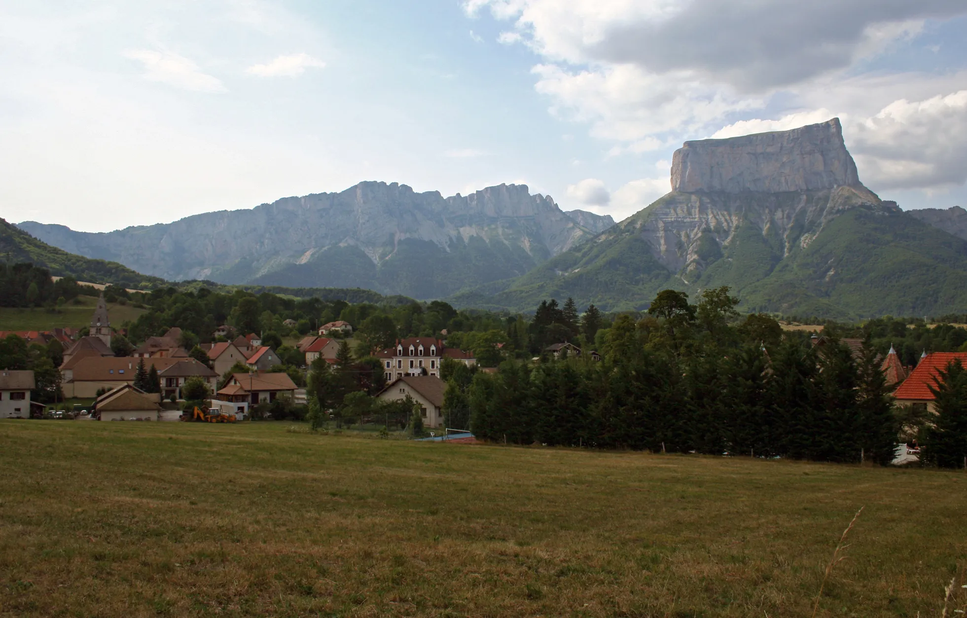 Photo showing: Mont Aiguille (Needle Montain) as seen from the Trieves. Mont aiguille is the mesa like mountain on the right. The cliffs on the left, called Rochers du parquet are the eastern limit of the Vercors plateau. The village of Chichilianne is visible in the foothills.