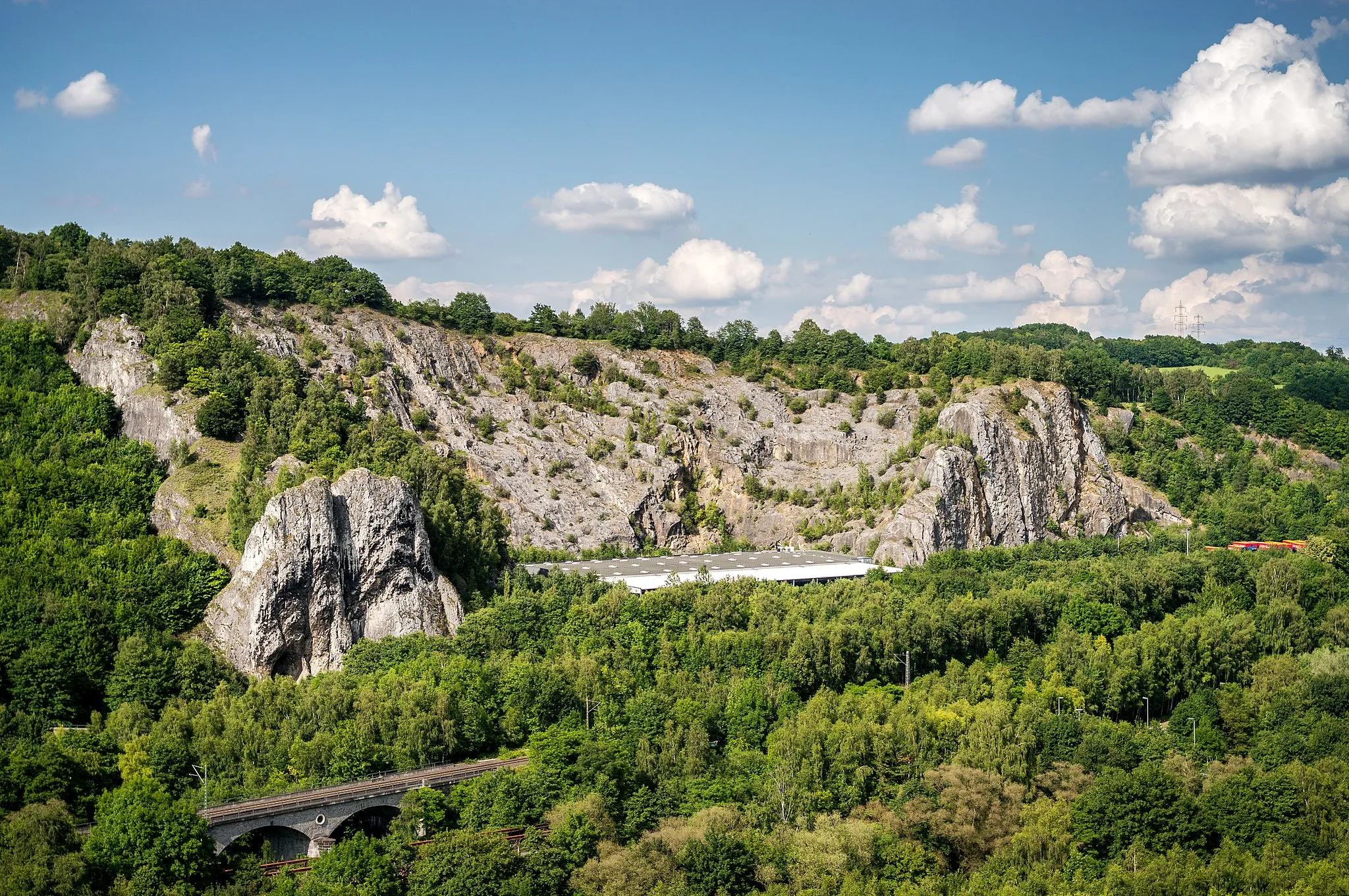 Photo showing: The southern flank of nature reserve Burgberg with its distinctive rock formation consisting of devonian compact limestone. On the left you can see the rock-natural monument "Pater und Nonne", which consists of two approximately 60m high rock towers. On its right side, you can see a part of the storage location of the shipping company Winner.