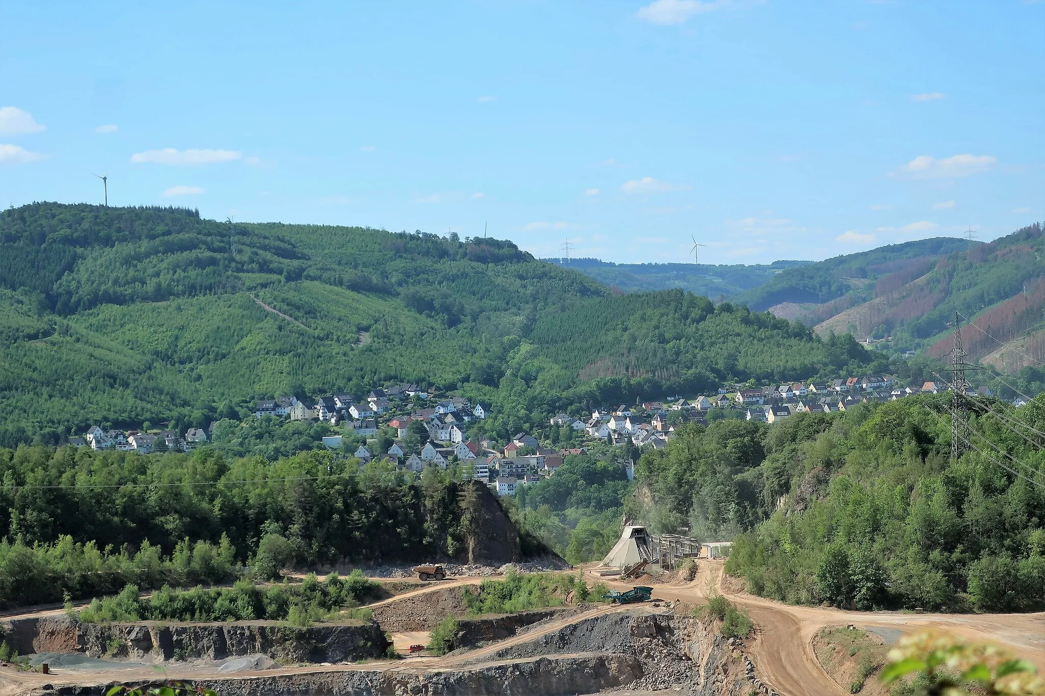 Photo showing: Landschaftsschutzgebiet „Roter Stein, Zimmerberg“ in Hagen-Hohenlimburg. Das große im Hintergrund liegende Waldgebiet mit wertvollem Baumbestand, östlich des Nahmertals (rechts), zwischen Lenne und Lahmen Hasen, ist mit zahlreichen Bächen durchzogen. Höchste Erhebungen: Zimmerberg (320 m) und Roter Stein (271 m). Vorne Steinbruch der Hohenlimburger Kalkwerke auf dem Gegenhang.