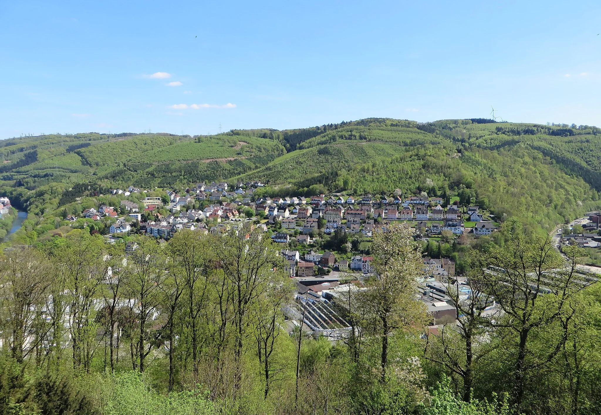 Photo showing: Blick von Schloss Hohenlimburg auf das Nahmertal im Hagener Stadtteil Hohenlimburg. Im Tal sieht man das Kaltwalzwerk C.D. Wälzholz, oberhalb der Häuser von „Bergholz“ und „Am Roten Stein“, das Landschaftsschutzgebiet „Roter Stein, Zimmerberg“. Das große Waldgebiet mit wertvollem Baumbestand, östlich des Nahmertals, zwischen Lenne (links) und Lahmen Hasen, ist mit zahlreichen Bächen durchzogen. Höchste Erhebungen: Zimmerberg (320 m) und Roter Stein (271 m).