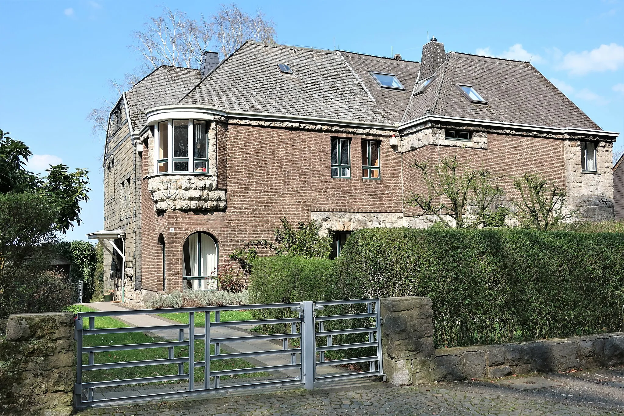 Photo showing: Blick auf die Villa am Stirnband 46 (links) in der Hagener Gartenstadt Hohenhagen (Eppenhausen). Außenfassade im Zusammenspiel von Bruchstein, Ziegelstein, Schiefer und dem architektonisch gelungenem Erker. 1910–1914 entworfen von dem holländischen Architekt J.L.M. Lauweriks.