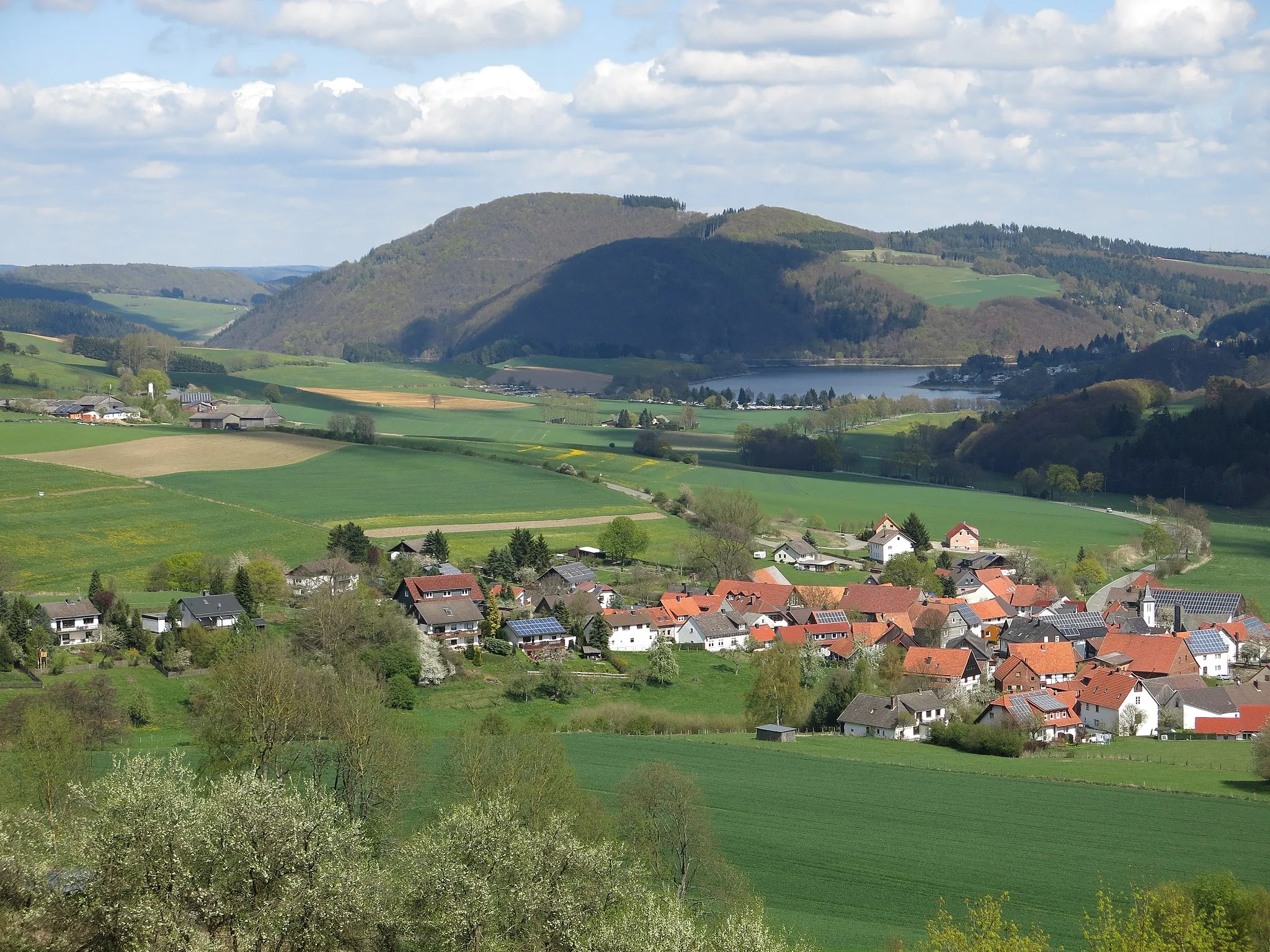 Photo showing: Blick vom Osthang des Koppen nach Nordosten zum Eisenberg (595 m). Davor ein Teil des Diemelsees und der Ortschaft Stormbruch.