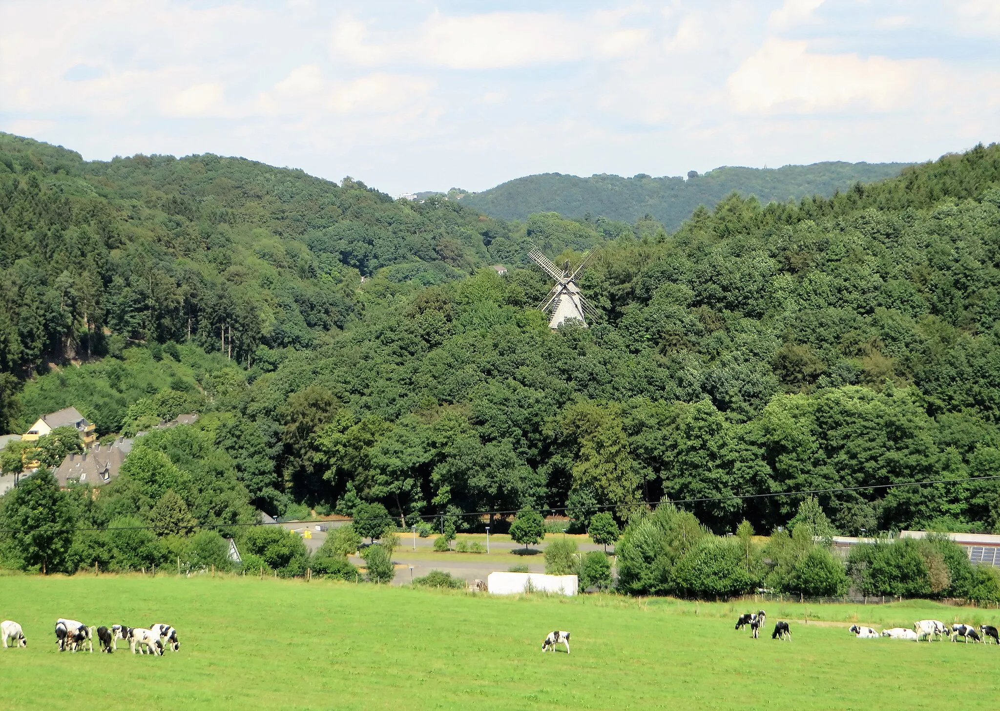 Photo showing: Blick vom „Alten Postweg“ in Hagen-Selbecke auf die Turmwindmühle des LWL-Freilichtmuseums Hagen (die Windmühle wurde 2021/22 abgebaut und in den hinteren Bereich des Freilichtmuseums umgesetzt). Der abgebildete Bereich zeigt zwei Bachtäler und die Grenzbereiche von drei Landschaftsschutzgebieten. Links über dem Selbecker Bachtal das LSG „Selbecke“. Die Windmühle oberhalb des Parkplatzes im Mäckinger Bachtal liegt im LSG „Eilper Berg/Langenberg“ und die Kuhweide „Auf dem Killing“ im Vordergrund gehört zum LSG „Rafflenbeuler Kopf“.