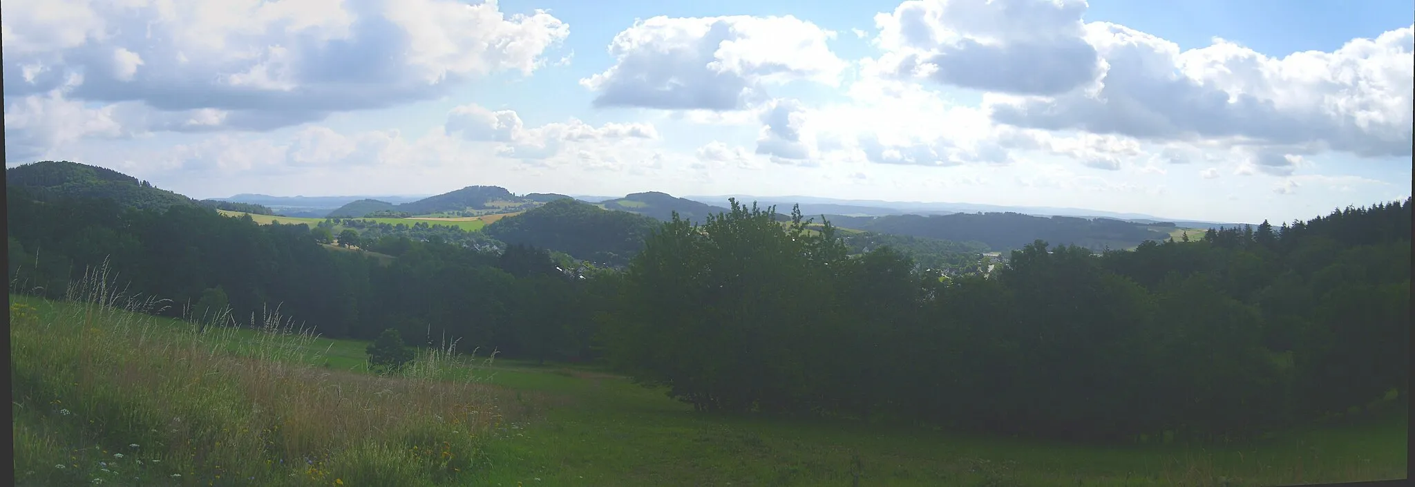 Photo showing: Blick von der Ostflanke des Hilmesbergs (635 m) an der Auffahrt zum Bollerberg (758 m); links der Stolzenberg (624 m), von dem aus sich die unbewaldete Niedrigwasserscheide zwischen Nuhne und Orke zu Stemmberg (572 m, halblinks) und Linsenberg (566 m, Mitte) zieht, nördlich deren das Hallenberger Hügelland in die Medebacher Schiefe Ebene übergeht. Rechts der Bildmitte Hesborn, dahinter der bis 530 m hohe Grat des Galgenbergs. Rechts des Stolzenbergs im Hintergrund der Eisenberg (560 m; 18,6 km), der jedoch größtenteils vom Eschenberg (535 m; 13,9 km) verdeckt wird, rechts davon der Nebengrat Böhlen (495 m; 15,5 km). Im Hintergrund der rechten Bildhälfte der Kellerwald, von dem besonders das Hohe Lohr (657 m; 31,5 km) hervorsticht.
– siehe Udeuschle