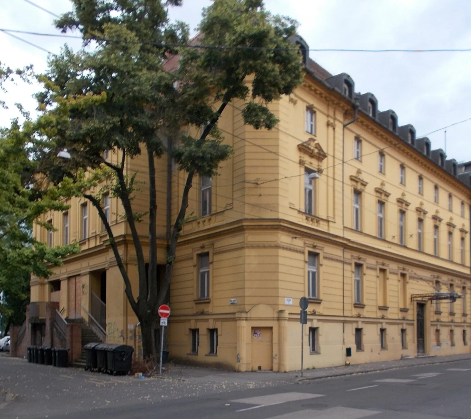 Photo showing: Two storey, three facades, listed corner building. Part of three cultural heritage ensembles. Built in 1897 as a one storey residential, community? café building to János Kass. Planned by Antal Steinhardt. Here was eight rooms flat of János Kass. Till 1920s here was Lloyd Association (pre Chamber of Commerce) event venue? and office. Built with arcades on Arany Street side. The courtyard was covered with iron glass roof based plans of the structural office of Schlick's iron foundry and machine factory in 1899. In 1911 on Stefánia side  a cellar was established with a cast slab designed by István Kopasz. Remodelled to hotel designed by architect Lipót Baumhorn and executed by János Kopasz in 1916. In 1952 the cellar and basement were remodeled according to the plans of József Barna. In 1977 the hotel was closed. The South Hungarian Building and Civil Engineering Company (DÉLÉP) bought it to transform the restaurant part into a community centre and the hotel into a guest house. Then it is owned by Hungária Rt. as Hungária Hotel. Since 1997, it has been owned by the Quaestor Group, which went bankrupt in 2015. In 2023, the building looked abandoned. - 2-4 Arany János utca=1-3 Dózsa Street = 8 Stefánia, Belváros (Inner City) neighborough, Szeged, Csongrád-Csanád County, Hungary.