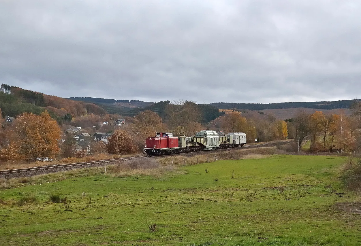 Photo showing: Ein Trafo-Schwertransport für die Firma Amprion, bestimmt für das Umspannwerk Dauersberg, mit einer Diesellokomotive der DB-Baureihe V100 auf der Hellertalbahn bei Zeppenfeld (November 2018).