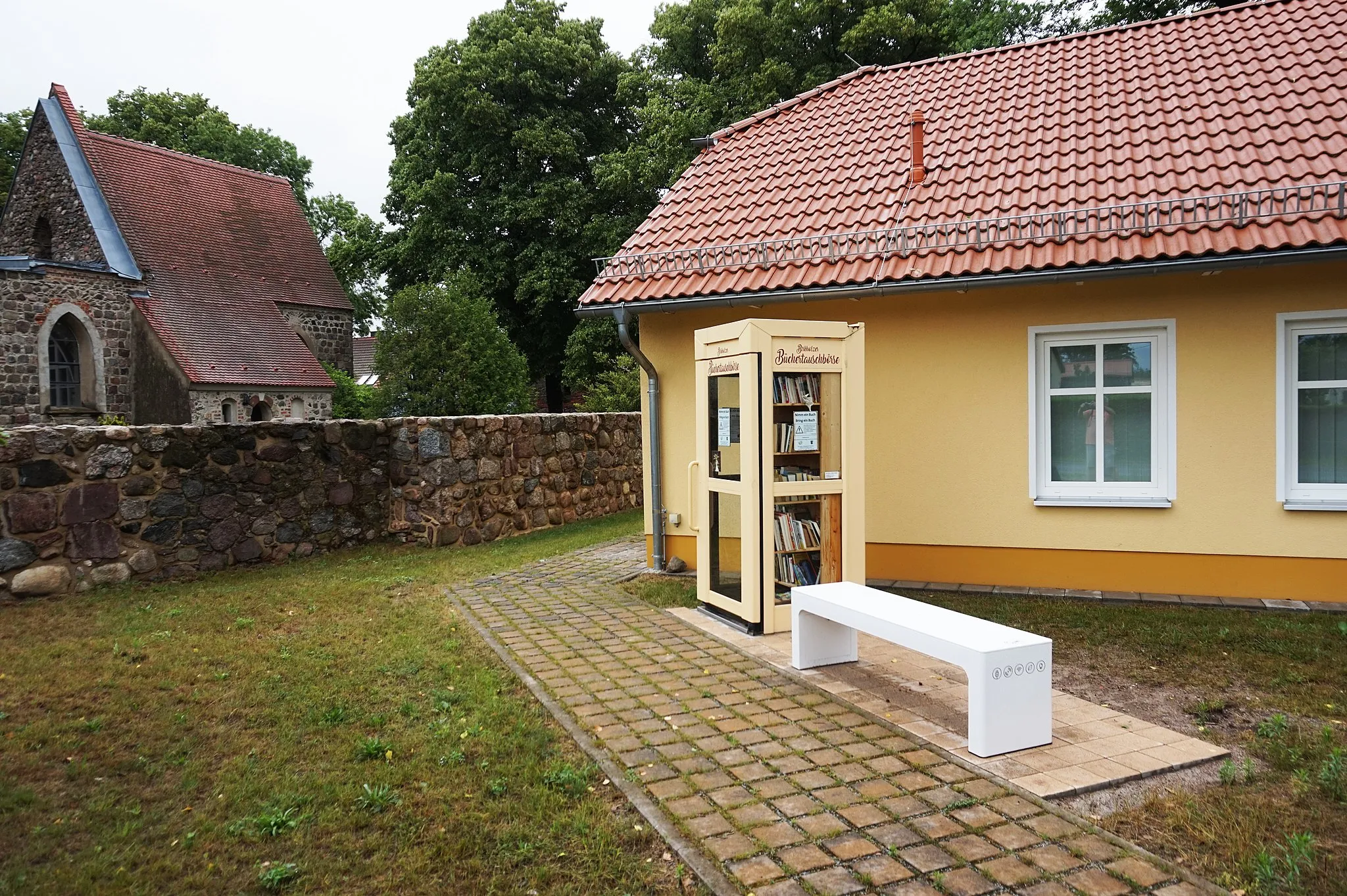 Photo showing: Kirche, Dorfgemeinschaftshaus, Büchertelefonzelle und Wlan-Bank auf dem Dorfanger von Birkholz 2021