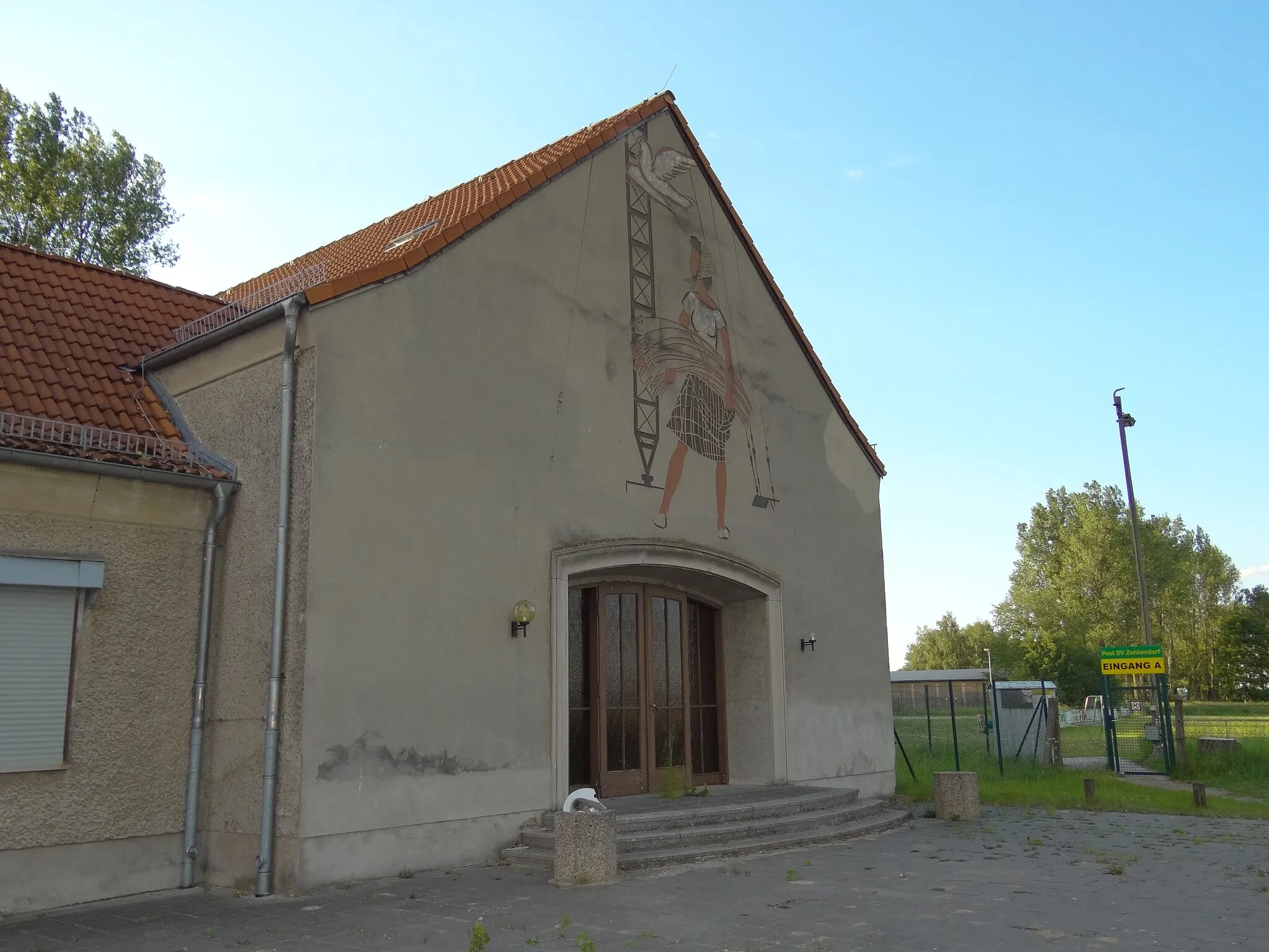 Photo showing: The entrance of, and a social realism mural on, the administration building of Sender Zehlendorf, a transmission site for long wave and medium wave radio, in the village of Zehlendorf bei Oranienburg which is under the administration of the city of Oranienburg in Brandenburg, Germany.