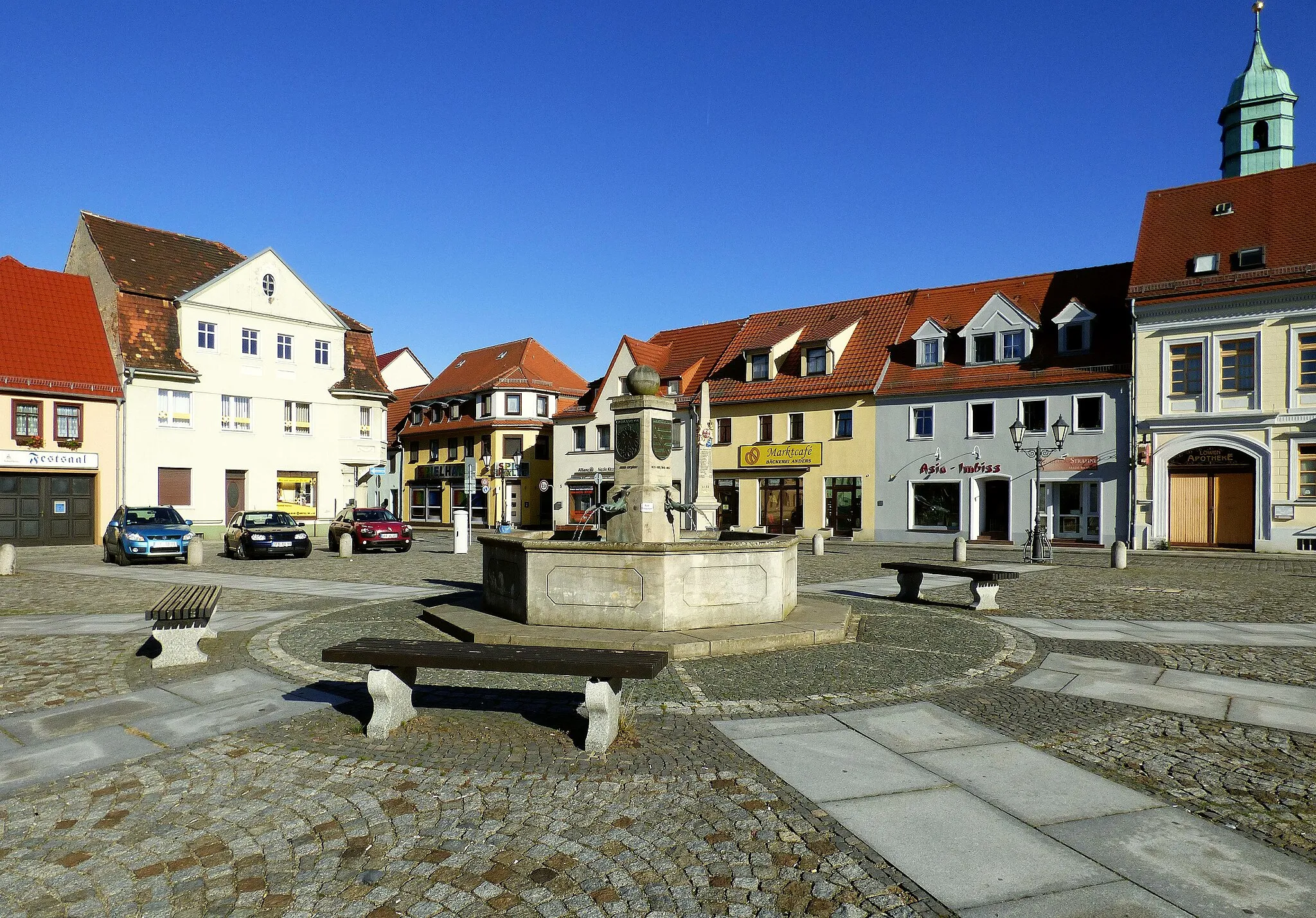 Photo showing: Marktbrunnen in Ruhland, Südwest-Ansicht; rechts Apotheke, hinten halbrechts in die Kirchgasse und halblinks Berliner Straße