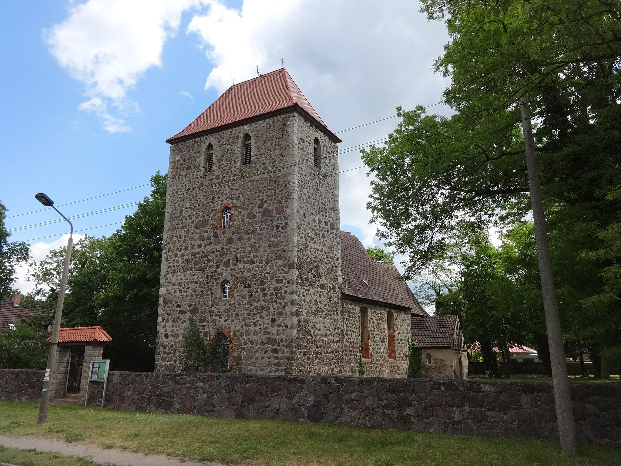 Photo showing: Die Kirche Rehfelde ist eine Chorquadratkirche, die in der zweiten Hälfte des 13. Jahrhunderts als regelmäßig geschichteten Feldsteinen errichtet wurde. Der Turm entstand zu einem späteren Zeitpunkt. In der flach gedeckten Kirche befinden sich eine Kanzel, ein Altar sowie eine Orgelempore aus dem Jahr 1722 sowie eine pokalförmige Fünte aus Rüdersdorfer Kalkstein