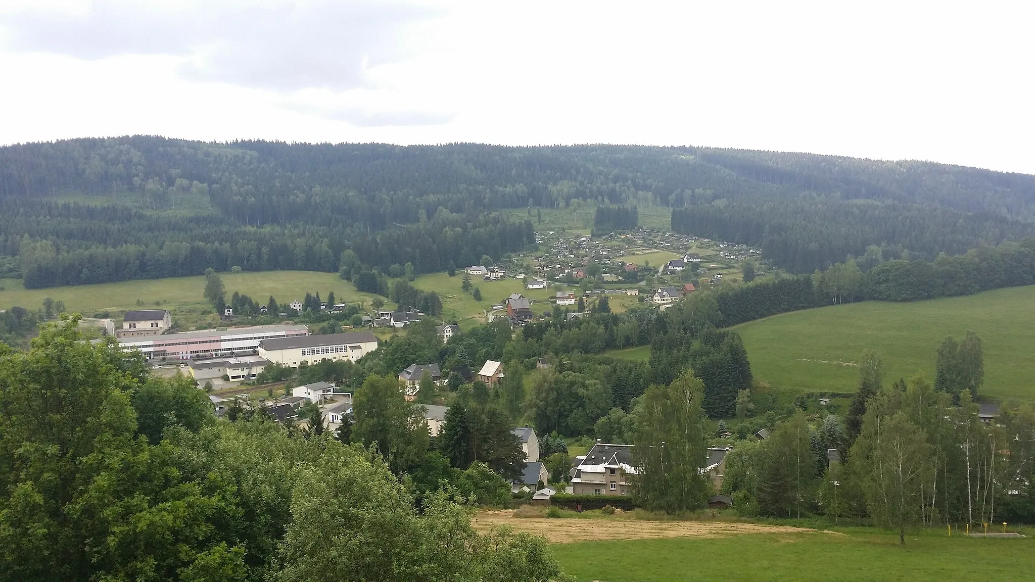 Photo showing: Blick in Richtung SSW aus Richtung An der Huth.
Vordergrund: ehem. Skipiste "Jägerlift" (Ausläufer), Miets- und Privathäuser, sowie Schrebergärten an der Jägerstraße, dahinter Ausläufer des Schwarzbergs, dahinter Klingenthal OrtsTeil Zwota K.O.T.Z..
Talwärts der Holzbau Klingenthal, die Bahnverbindung Sokolov-Oberzwota (nicht eindeutig erkennbar parallel der Bach Zwota, welcher auf tschechischer Seite in die Eger und somit später in die Elbe mündet), die ehemalige Stadthalle Klingenthal (nunmehr Einkaufszentrum) und die Klingenthaler MaschinenWerke KMW.

Im Hintergrund der Barthelsberg mit Erlbacher Straße, an welcher ebenfalls eine Schrebersiedlung und private Wohnhäuser liegen.