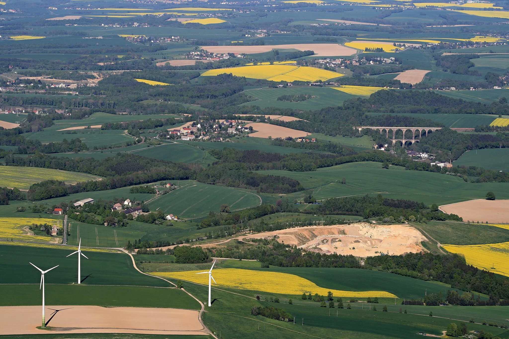 Photo showing: Sächsische Landschaft im Bereich der Gemeinden Lunzenau und Wechselburg, Landkreis Mittelsachsen, Sachsen. – LSG c01 „Mulden- und Chemnitztal“ in der Bildmitte, ein Teil des Windparks Elsdorf vorne links, Sand- und Kiesgrube Bergmann vorne rechts, Göhrener Viadukt rechts.