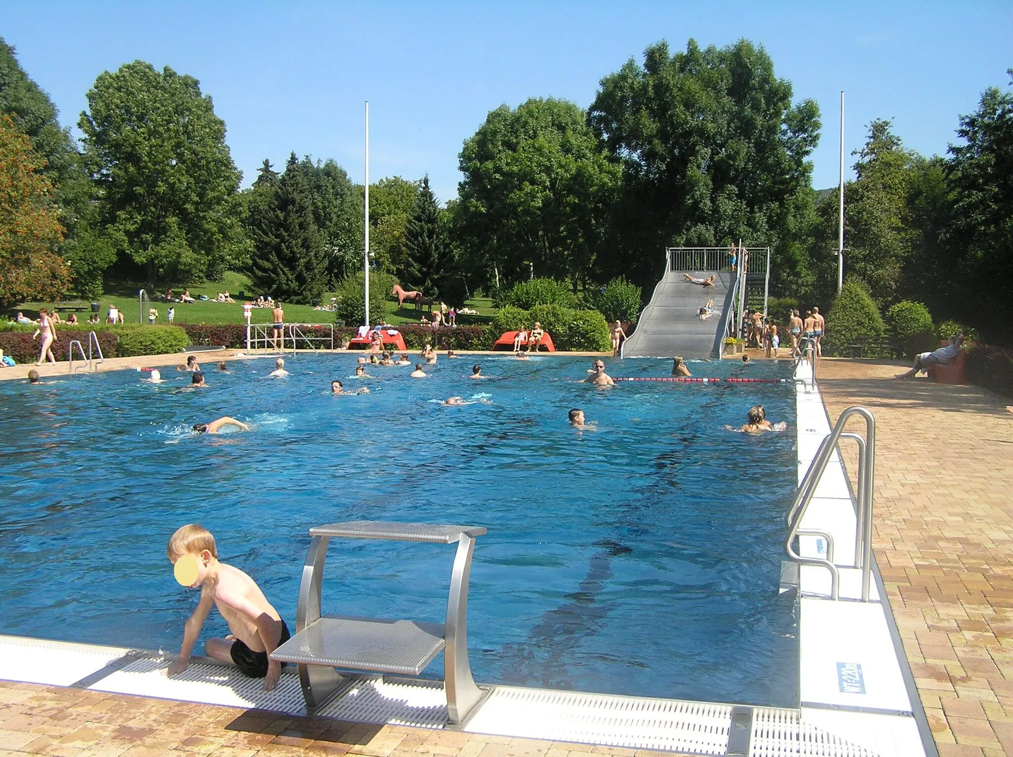 Photo showing: Freibad in Schloßborn. Das Bild zeigt das große Becken mit der Rutsche. Im Hintergrund sind die Liegewiesen und die Kletterpferde zu sehen