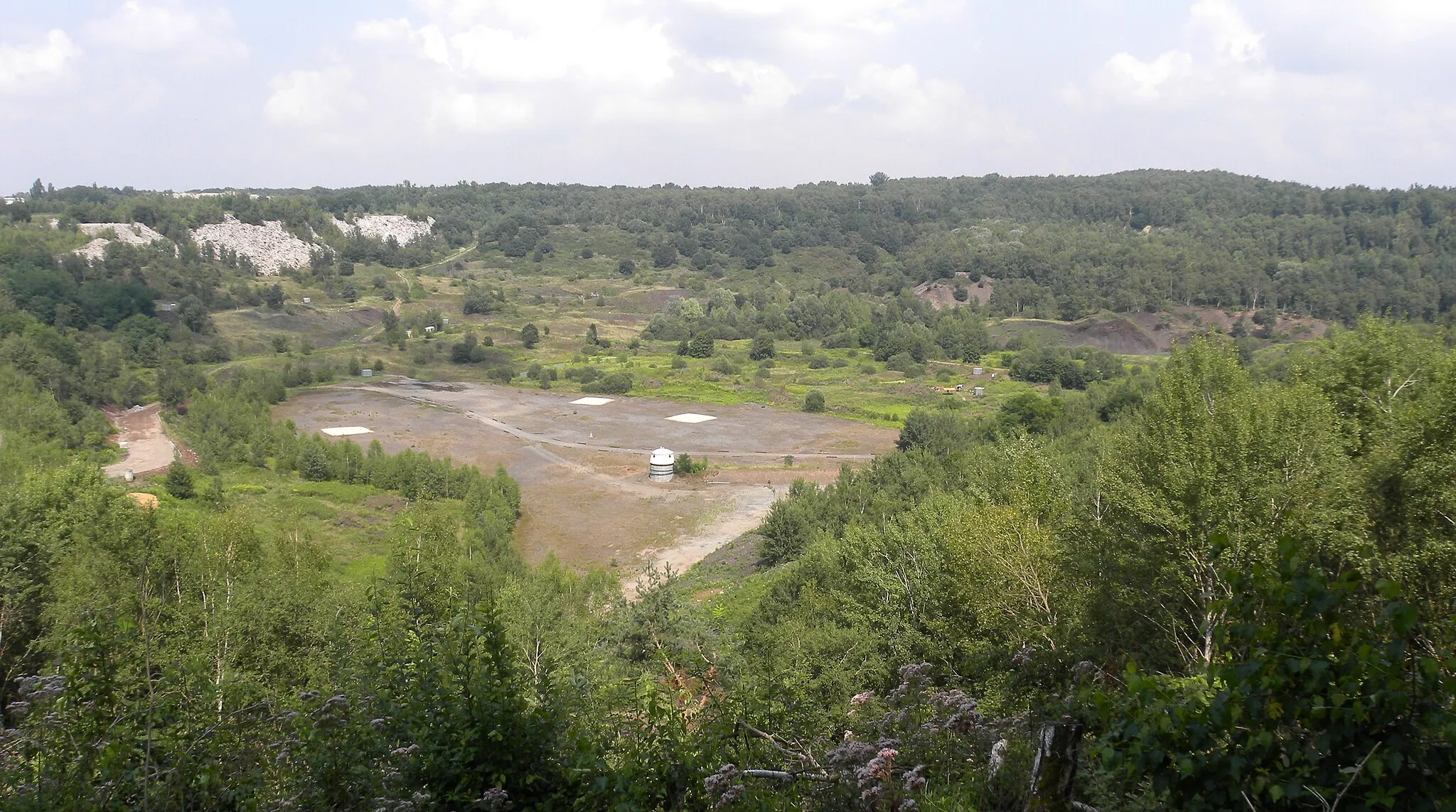 Photo showing: Messel Fossil Pit (Eocene, Germany), viewed from its southern rim with view to the northeast. The whitish slopes on the left (north) belong to the waste dump of the nearby factory of the Ytong company.