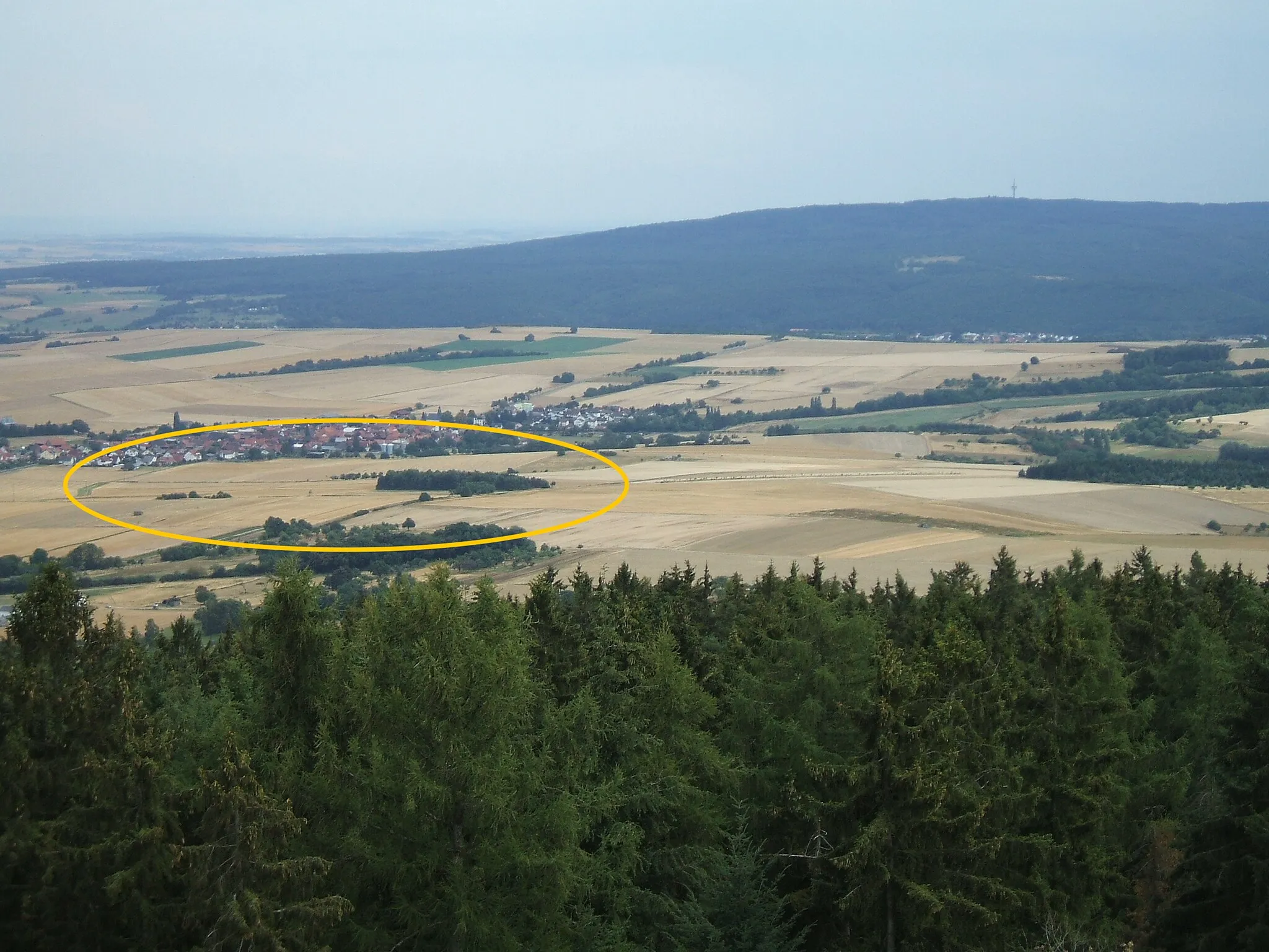 Photo showing: Blick vom Aussichtsturm auf dem Hausberg auf Fauerbach v.d.H. und die Landschaft nördlich (davor), in der die beiden Äste des Riedgrabens liegen, hervorgehoben durch das ockerfarbene Oval. Etwa in der Mitte des Bildes verläuft die K 15 von links, Hoch-Weisel, nach rechts, Münster. Im Hintergrund rechts ist der Steinkopf mit seinem Fernmeldeturm.