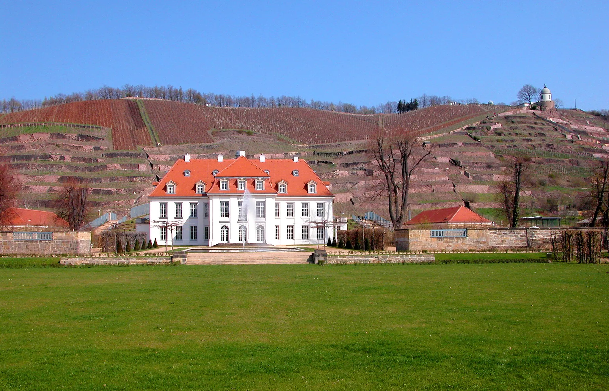 Photo showing: 10.04.2004  01445 Radebeul, Wackerbarthstraße 1: Barockschloß Wackerbarths Ruhe (GMP: 51.114344,13.618261), heute Sächsisches Staatsweingut Schloß Wackerbarth. Haupthaus, erbaut 1727-29 nach Plänen von Landesbaumeister Johann Christoph Knöffel als Alterssitz für den Minister Augusts des Starken, den Reichsgrafen Christoph August von Wackerbarth (1662-1732). Dem Grafen war in der Niederlößnitz nur eine kurze Ruhezeit beschieden. Er starb 1734. Das Schloß Wackerbarths Ruhe ist eigentlich kein Schloß, da mit dem Anwesen keine herrschaftlichen Rechte verbunden waren. Es handelt sich vielmehr um ein sehr groß ausgefallenes Herrenhaus eines Weinguts. 1853 stark verändert. Das Weingut geht auf das 1952 in Radebeul gegründete Staatsweingut sowie das 1992 entstandene VEG Weinbau Radebeul zurück. Bis 1957 wurden hier nur Weine gekeltert, 1958 begann auch die Herstellung von Sekt. Das Schloß Wackerbarths Ruhe ist das größte und wohl auch schönste historische Weingut in Sachsen. Daß man Wackerbarths Ruhe heute wieder in einem Zustand erleben kann, der dem des 18. Jahrhunderts nahe kommt, ist dem kunstsinnigen Fabrikanten Alfred Tiedemann (18751962) zu verdanken. Dieser ließ Herrenhaus und Garten ab 1916 durch den Dresdner Architekten Georg Heinsius von Mayenburg (1870-1930) instand setzen. Ansicht von Süden. Auf dem Berg der Jacobstein, 1743 vom Hofböttcher Jacob Krause erbaut.                                    [DSCN2708.TIF]20040410100DR.JPG(c)Blobelt