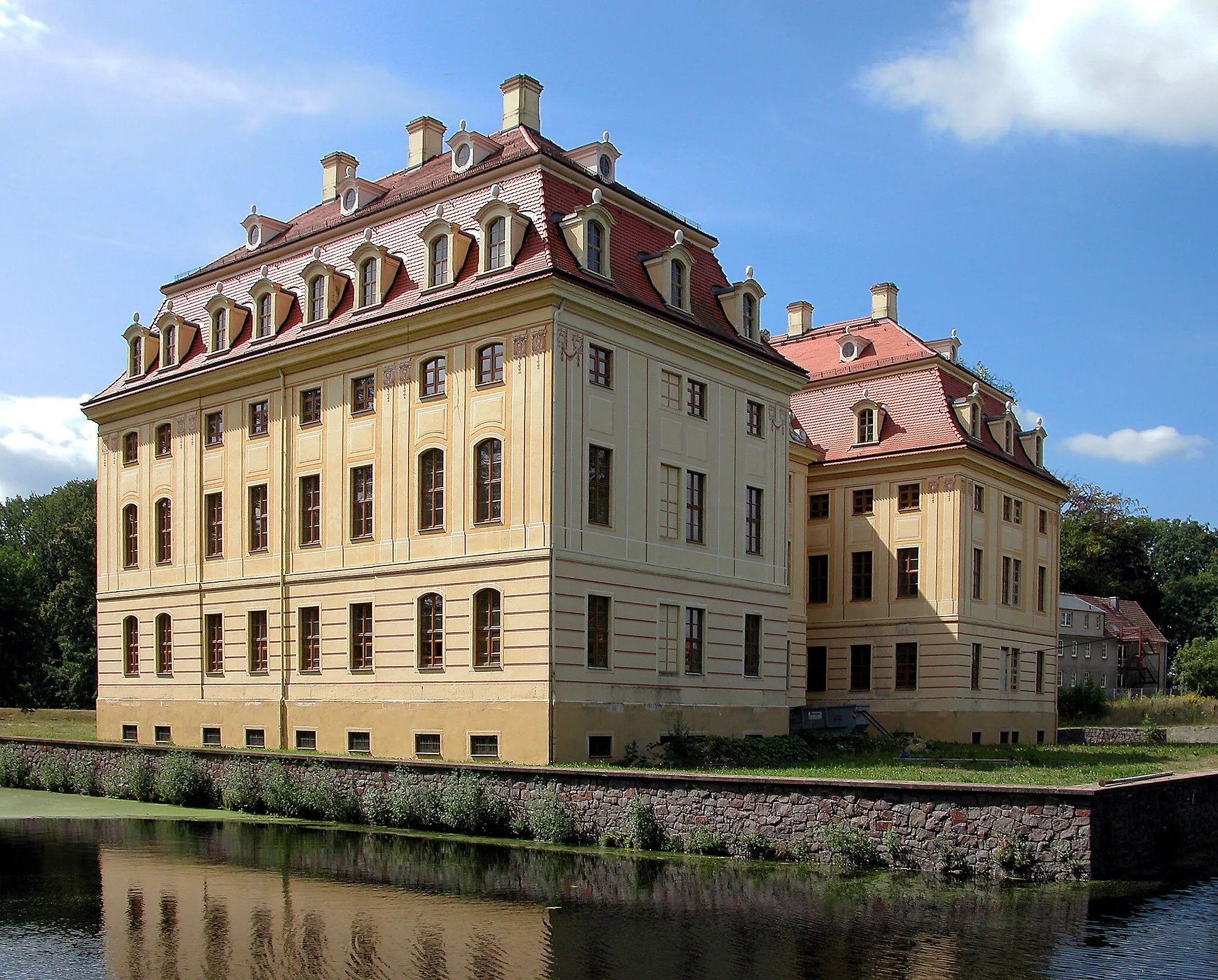 Photo showing: 16.08.2003   01454  Wachau, Am Schloß 1 (GMP: 51.158825,13.903120): Wasserschloß,  errichtet 1730-1754 auf älterer Grundlage für Johann Georg von Schönfeld. Ab 1800 im Besitz der Herren von Oppel. In der DDR-Zeit sind im Schloß Wohnungen, eine Arztstation, das Standesamt, die Bücherei, der Schulhort und zwei Verkaufsstellen. 1991-1998 werden Dach- und Fassaden saniert, die Fenster erneuert, der Schloßteich entschlammt und die Ufermauern neu errichtet. Sicht von Nordosten.                                                                                                                                                                                                            [DSCN]20030816240DR.JPG(c)Blobelt