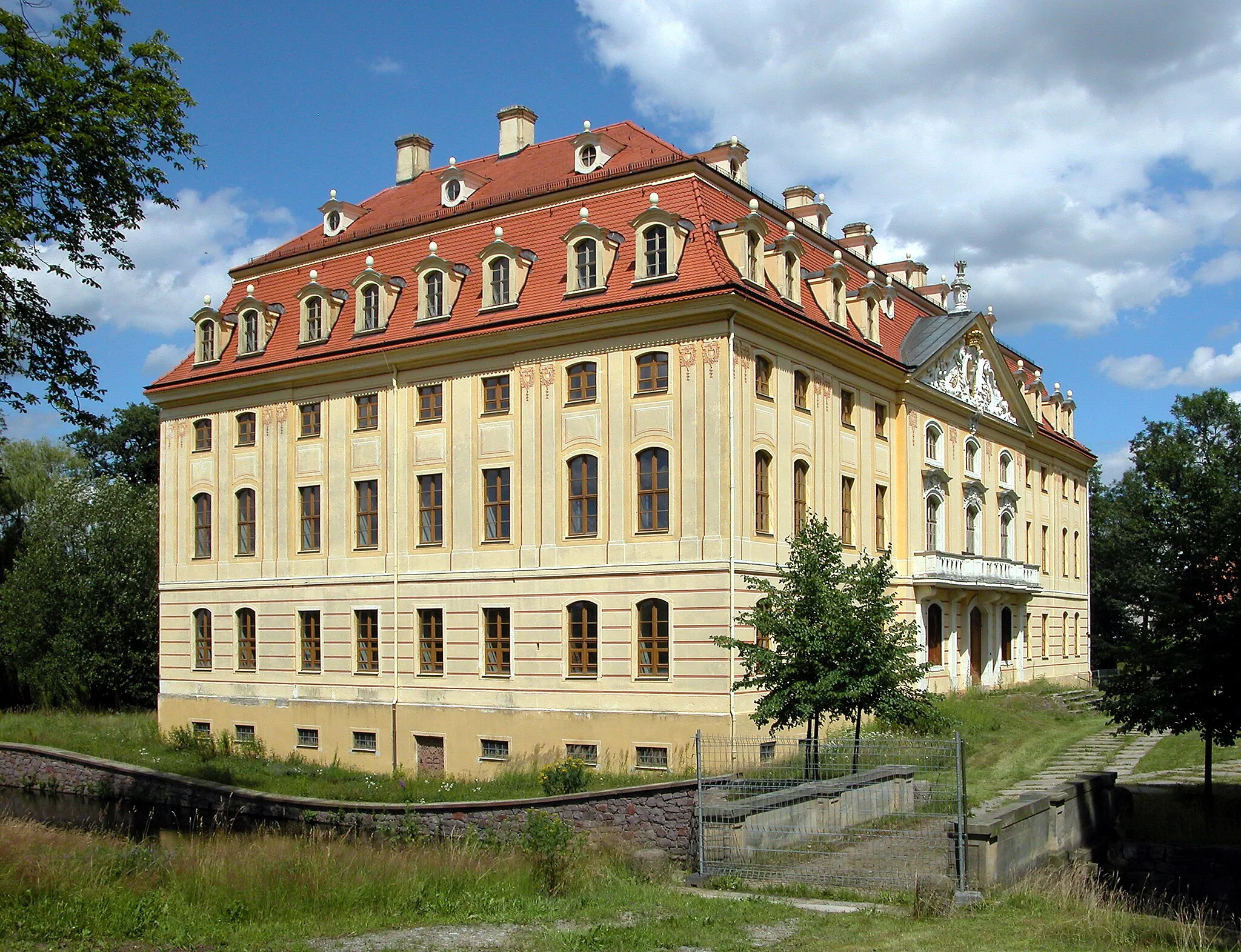 Photo showing: 09.07.2012  01454  Wachau, Am Schloß 1 (GMP: 51.158825,13.903120): Wasserschloß,  errichtet 1730-1754 auf älterer Grundlage für Johann Georg von Schönfeld. Ab 1800 im Besitz der Herren von Oppel. In der DDR-Zeit sind im Schloß Wohnungen, eine Arztstation, das Standesamt, die Bücherei, der Schulhort und zwei Verkaufsstellen. 1991-1998 werden Dach- und Fassaden saniert, die Fenster erneuert, der Schloßteich entschlammt und die Ufermauern neu errichtet. Ansicht Parkseite. [DSCNn4311.TIF]20120709220DR.JPG(c)Blobelt