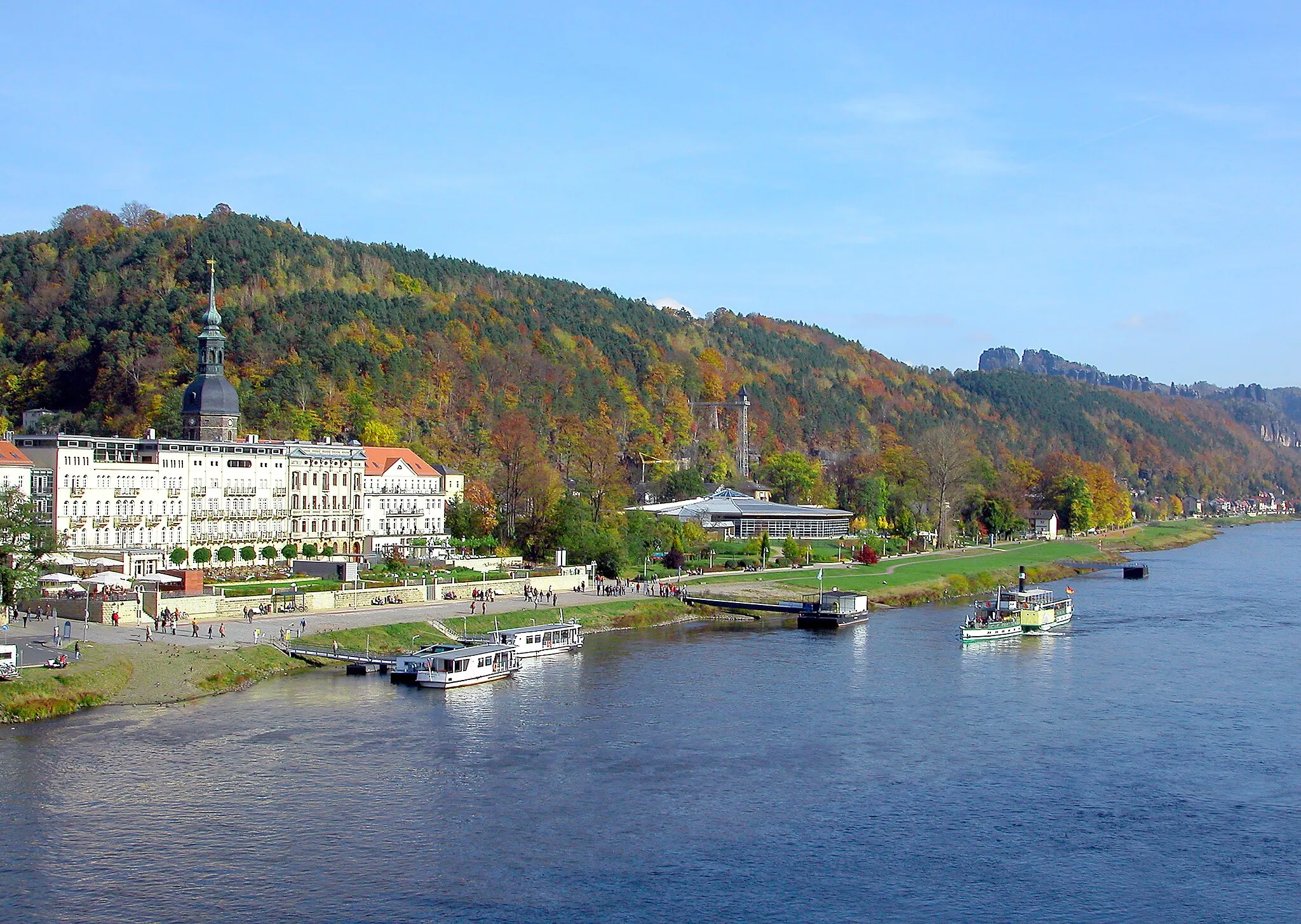 Photo showing: 18.10.2008   01814  Bad Schandau: Blick von Süden über die Elbe nach Bad Schaudau auf die Hotels an der Elbpromenade (GMP: 50.017068,14.153628) zwischen der Königsteiner Straße und der Dampfschiffstraße. Überragt werden die Promenaden-Hotels vom Turm (1711) der Johanniskirche. Rechts die "Toskana Therme" (GMP: 50.916536,14.156195). 1999-2002 erbaut als Kurmittelhaus durch die Kurortentwicklungsgesellschaft, im März 2002 als "Schrammsteinbad" eröffnet. Nach Hochwasserschäden und Wiederaufbau Eröffnung als Toskana Therme. Dahinter der historische Aufzug (GMP: 50.916712,14.161279) zur Ostrauer Scheibe. Der Hotelier Rudolf Sendig ließ 1904/05 diesen Turmaufzug von der Aufzugsfirma Kühnscherf & Söhne aus Dresden konstruieren. Die Stahlkonstruktion wurde von der Firma Kelle & Hillebrand aufgestellt. Der Ingenieur war ein Schüler Gustav Eiffels. Am rechten Horizont das Schrammsteinmassiv, das nach links mit dem Torstein (425 m) endet. Links davon der dominante Falkenstein (381 m).                                                                                                                                                                                                                        [DSCN34738.TIF]20081018340DR.JPG(c)Blobelt