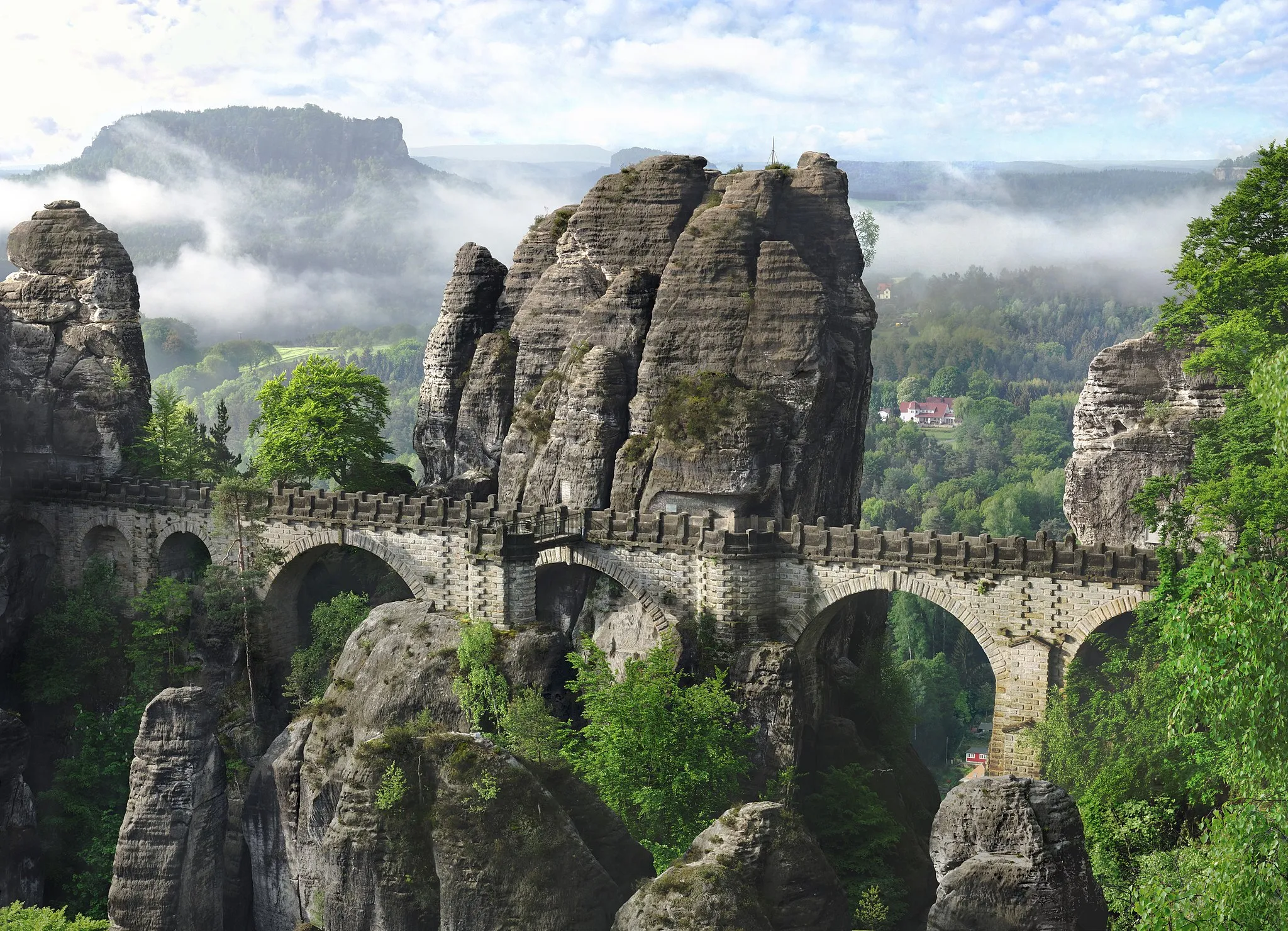 Photo showing: The picture shows the Bastei Bridge morning in the mist.
This bridge is 76.5 meters long and crosses the Martertelle. It creates a link between the Neurathen Castle and the Bastei at an altitude of 165 meters above the river Elbe. It was built in the years 1850/51 and has become the symbol of the Saxon Switzerland.