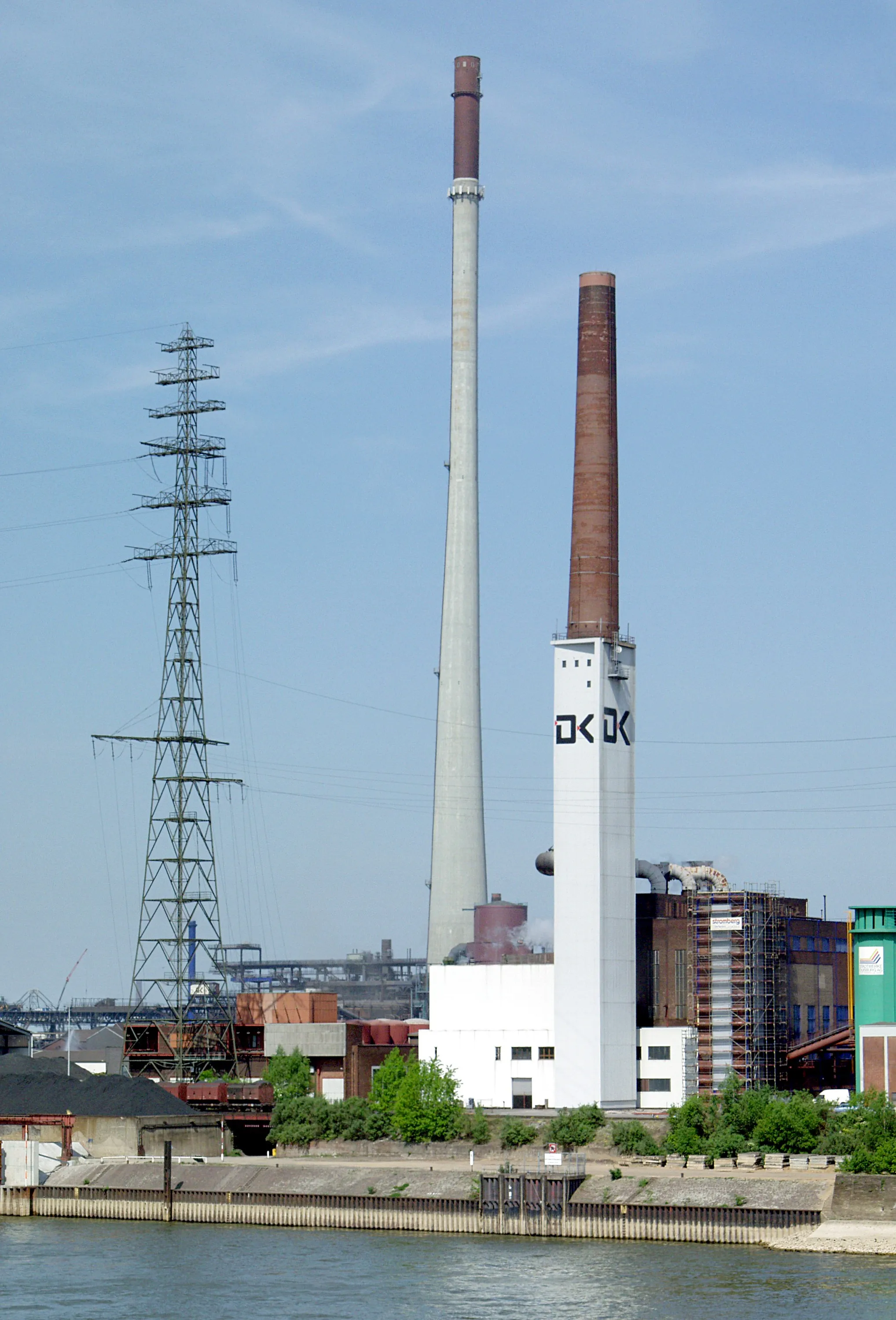 Photo showing: Rechtes Rheinufer Duisburg-Hochfeld. Links: Mast der Freileitungskreuzung (110 kV, Bl. 2303) über den Rhein, Mitte: Schornstein der Sinteranlage der DK Recycling GmbH. Höhe: 250 m