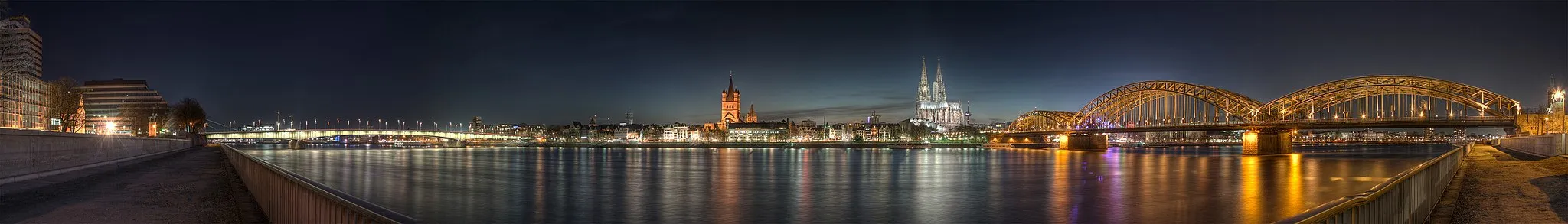 Photo showing: Panoramic view of the old town of Cologne (North Rhine-Westphalia, Germany) taken from the other side of the river Rhine at dusk (09:58pm). You can see (from left to right) the former Lufthansa corporate headquarters, the Deutzer bridge, Great St. Martin Church, Cologne Cathedral, Museum Ludwig, the Cologne telecommunications tower Colonius, the Hohenzollern bridge and the blue lights and reflections of the Cologne Musical Dome.Five images with 3 exposures each (15 images in total) were merged together. The resulting 32bit HDRI was converted to an 8bit LDRI. Images were taken with a Canon EOS 1000D (EOS Digital Rebel XS or EOS Kiss F) and 18-55mm lens at f/5.6.