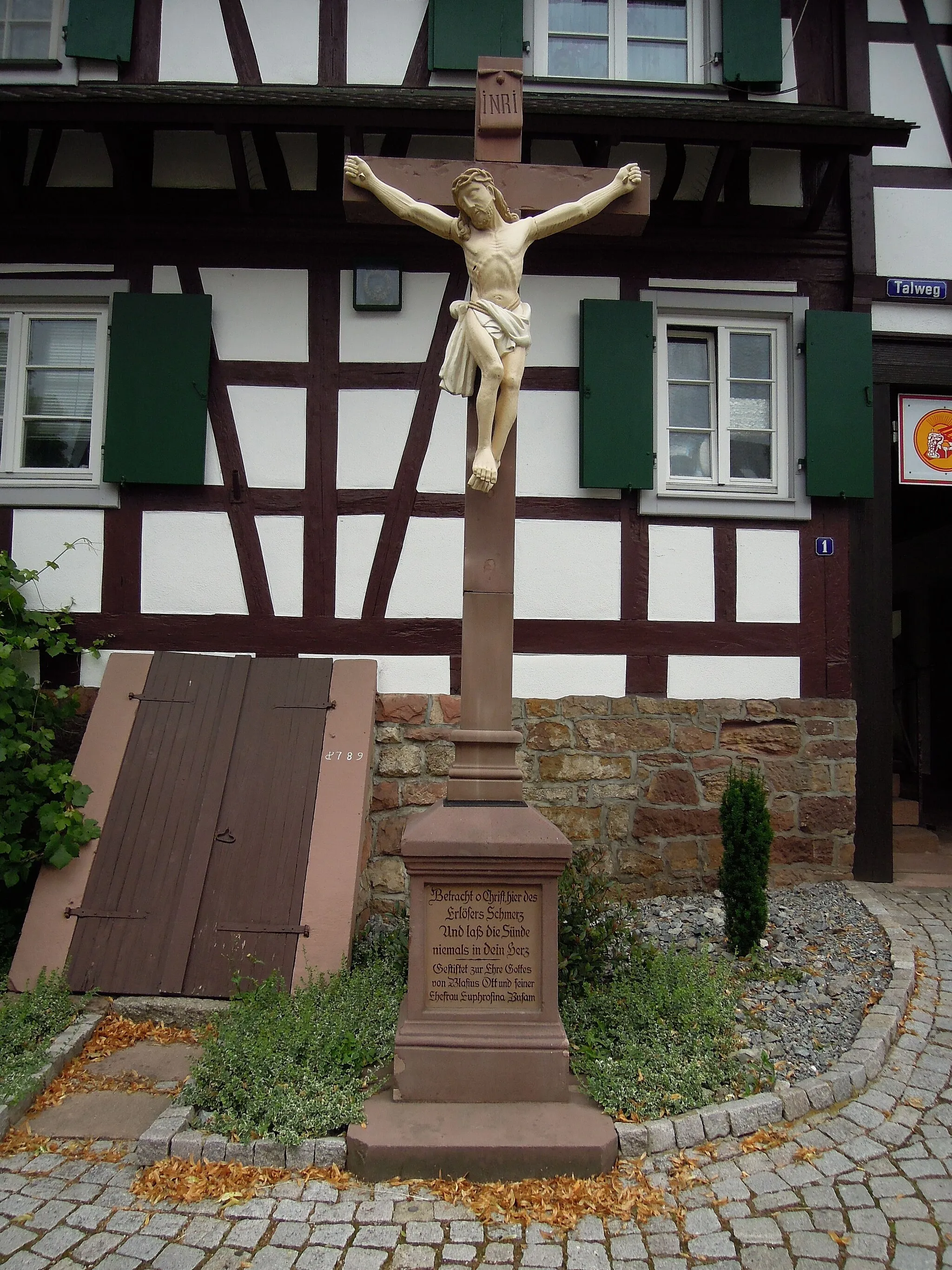 Photo showing: helle Christusfigur an rötlichem Sandsteinkreuz auf rechteckigem Sockel mit Inschrift