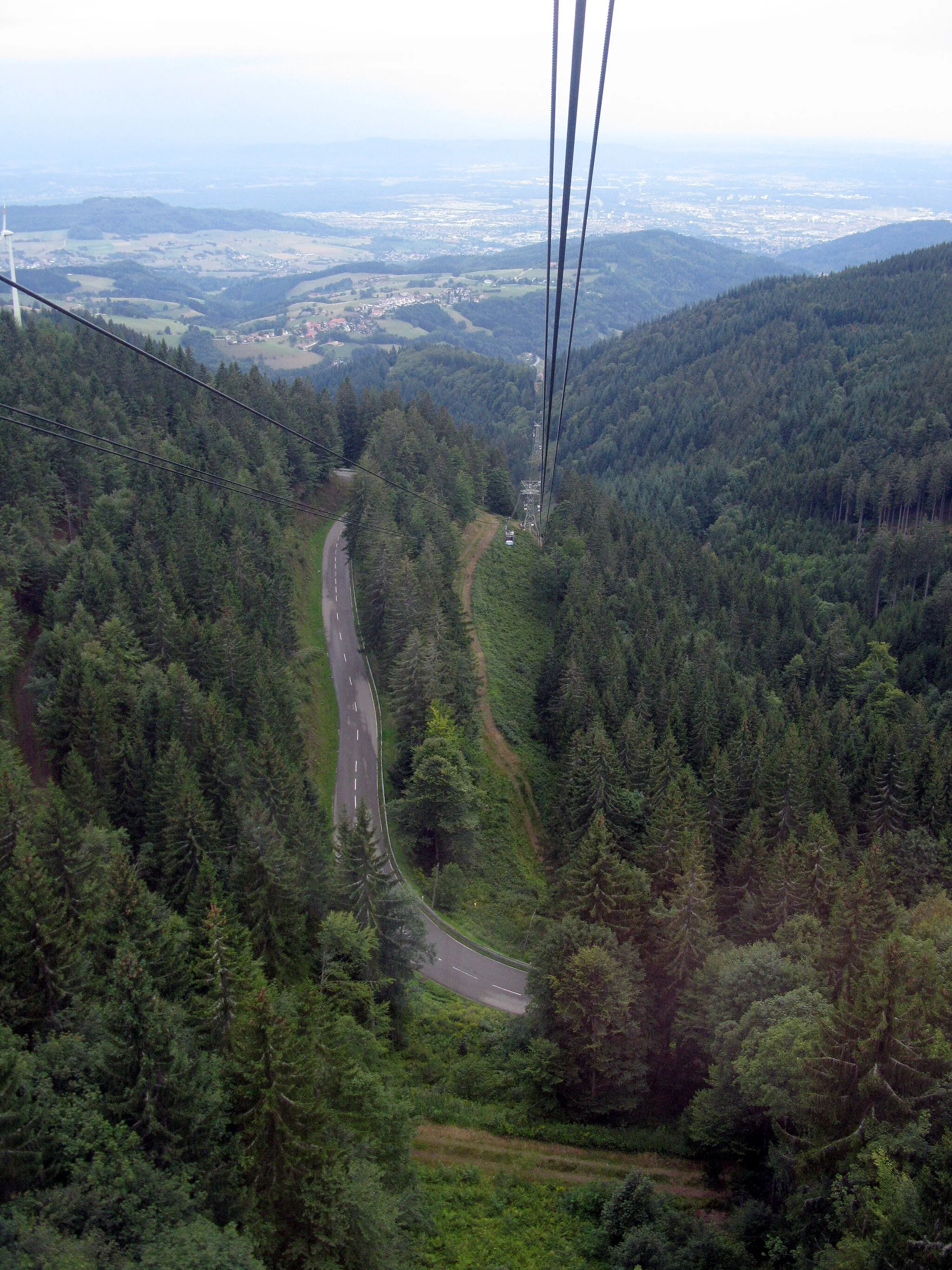 Photo showing: Blick von der Freiburger Schauinslandbahn auf die Schauinslandstraße oberhalb der Brünnelekurve, am linken Bildrand ein Windrad der Holzschlägermatte