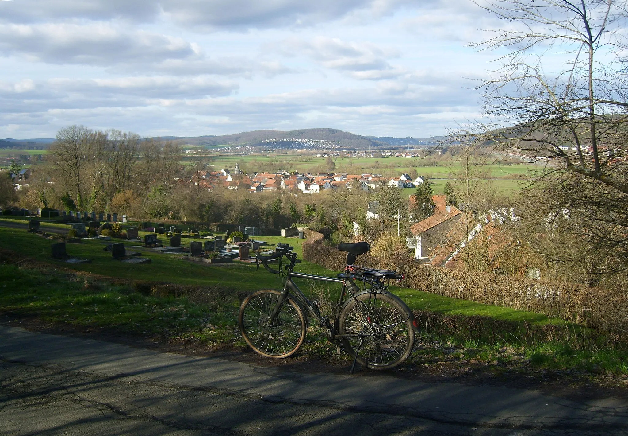 Photo showing: Blick vom Friedhof Roth am Geiersberg (223 m) auf den Marburger Rücken mit der Schneiße (327,1 m), dem das eigentliche Marburger Lahntal verriegelnden Weimarschen Kopf (305,4 m), der Kirchspitze (323,5 m) und dem gut erkennbaren Marburger Schloss (etwa 10 km entfernt), der nach rechts optisch in die zentralen Lahnberge übergeht; rechts im näheren Hintergrund der Rothlauf (287,4 m) in den südlichen (Nieder-)Lahnbergen. Am Weimarschen Kopf Niederweimar, rechts davor Argenstein, vor dem Rothlauf Wolfshausen, das durch die B 3a abgetrennt wird.
Im Vordergrund das Gravelbike CAADX 105 SE von Cannondale mit Alurahmen und Karbongabel in Vollausstattung.