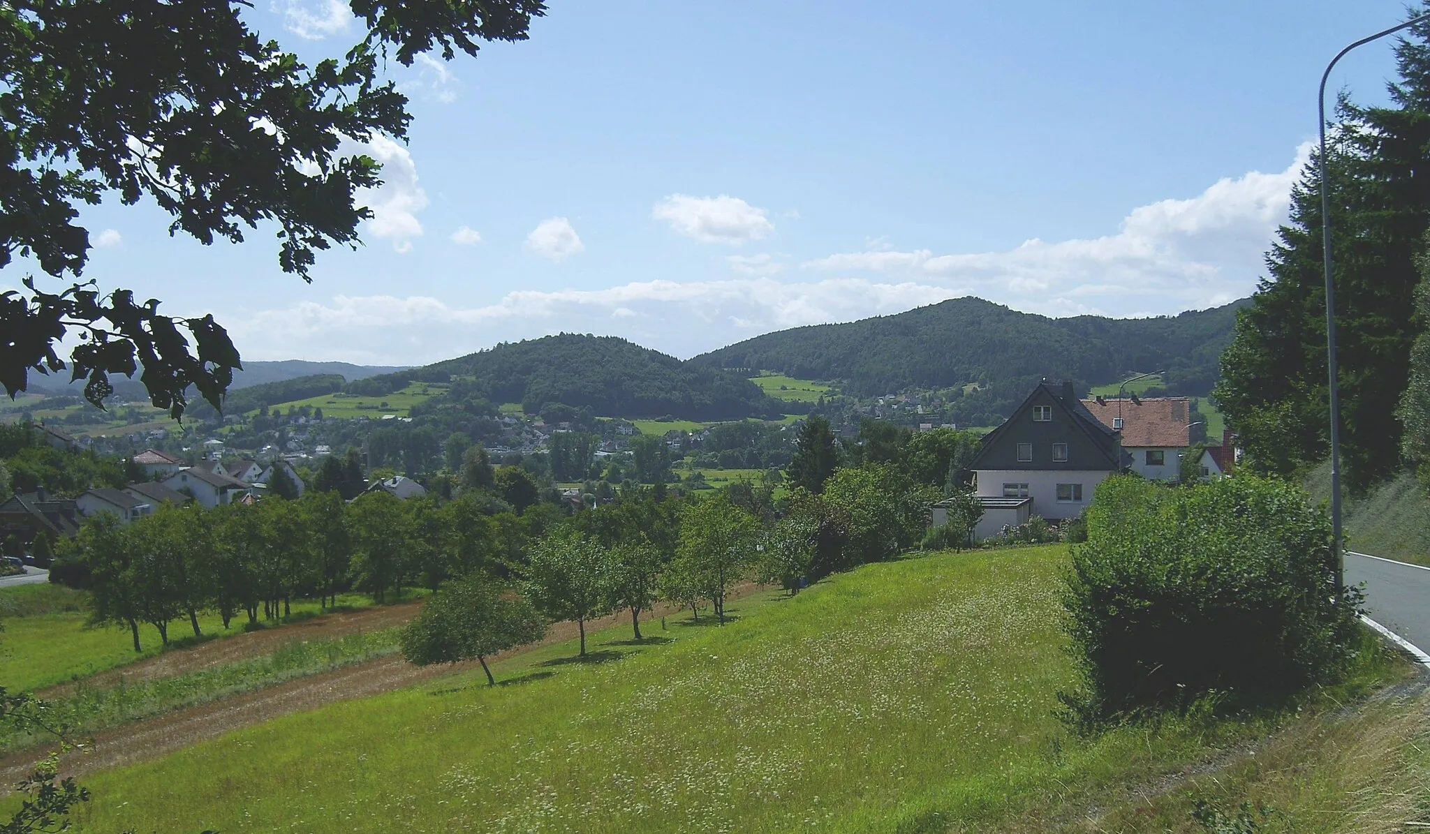 Photo showing: Blick vom Ortsausgang Richtung Katzenbach auf Kombach (Vordergrund), Wolfgruben (dahinter) und Dautphe-Wilhelmshütte (links davon); im Hintergrund die Südostausläufer des 561m hohen Schwarzenberges, nämlich der 378m hohe Roth (Mitte) und der 461m hohe Beilstein (rechts), an die sich noch weiter rechts der 533m hohe Nimerich anschlösse. Links, im ferneren Hintergrund, die Bottenhorner Hochflächen mit der 609m hohen Angelburg (Fernsehturm)