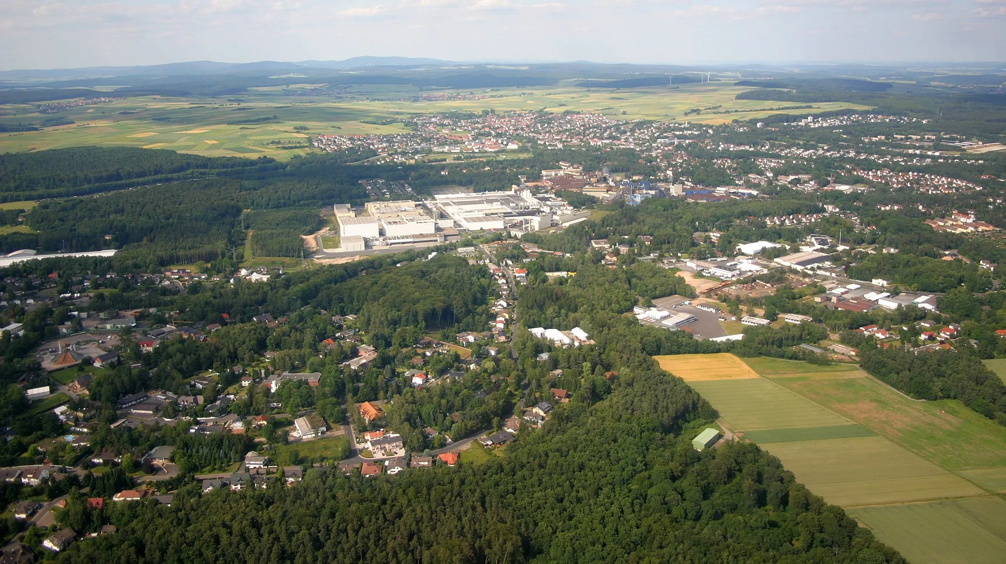 Photo showing: Stadtallendorf im Jahr 2004, fotografiert aus Richtung Westen. Im Foto zu sehen: Das Industriegebiet DAG mit dem Ferrero-Werk in der Bildmitte, der alte Ortskern ganz hinten, die Herrenwaldkaserne am rechten oberen Bildrand. Auf dem Foto wird die von großen Waldflächen durchzogene Bebauung deutlich.