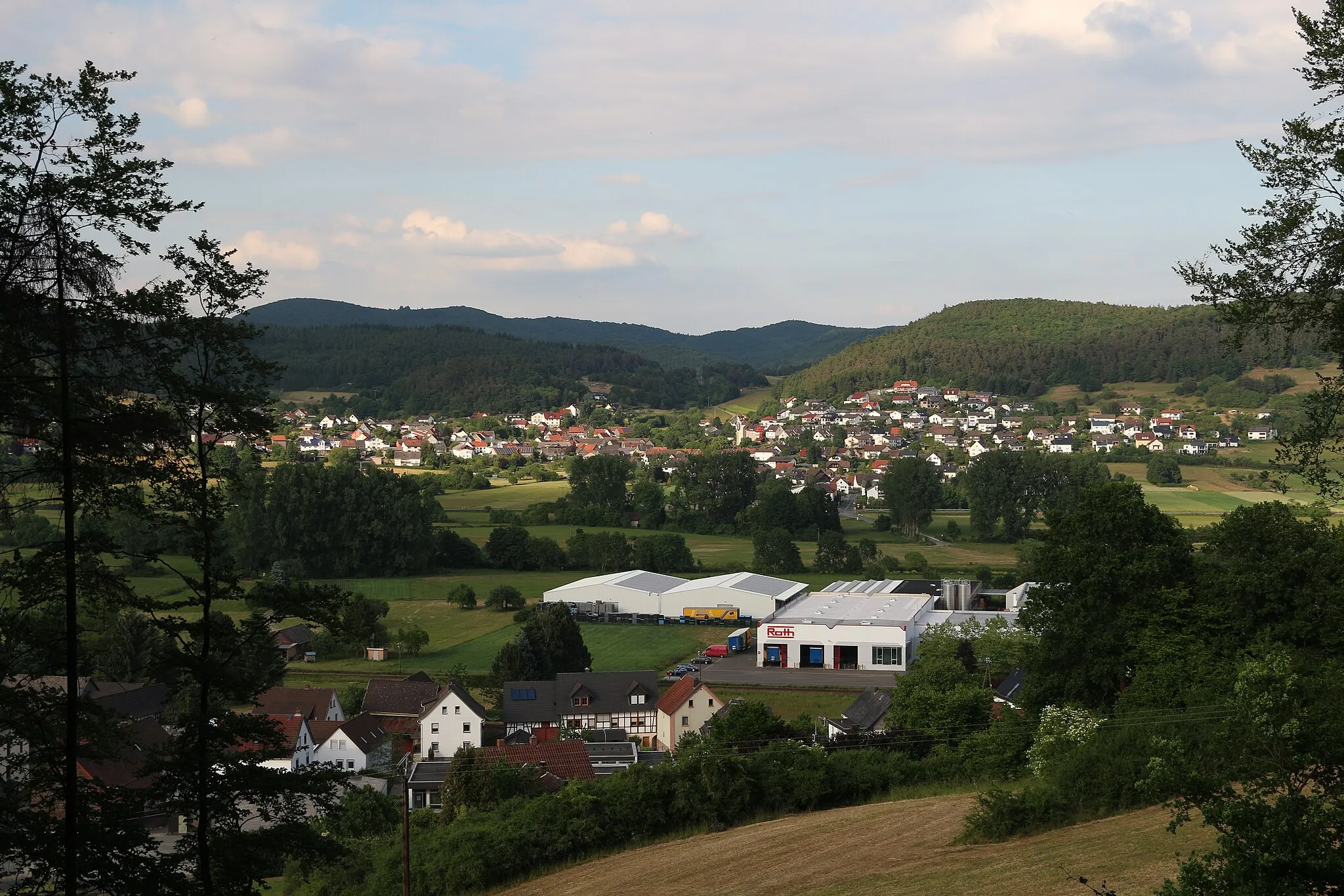 Photo showing: Kombach. Im Vordergrund Roth Kunststofftechnik (Lahnweg, 35232 Dautphetal-Wolfgruben). Direkt vor dem Werk vorläuft die de:Bahnstrecke Kreuztal–Cölbe (Obere Lahntalbahn). Wenige Meter hinter dem Werk fließt die Lahn.