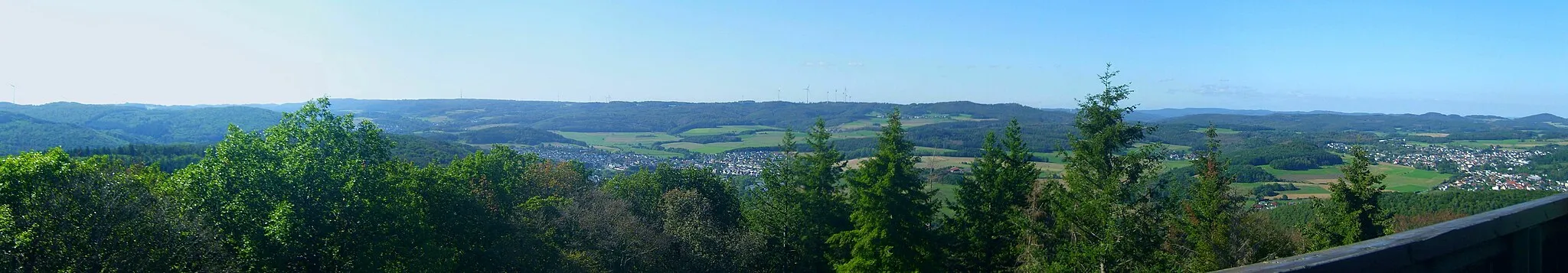 Photo showing: Blick vom Koppeturm im Höhenzug Zollbuche bei Erdhausen auf die Bottenhorner Hochflächen; rechts der Rimberg (498 m; 12 km entfernt), links davon die Kappe (494 m; 11,3 km); weiter links und eine Reihe dahinter Arennest (592 m; 19,4 km) und Sackpfeife (674 m; 23,6 km) nebst Hainpracht (631 m; 22,3 km), links davon wird der Buchholz (643 m; 25 km) von einem Weihnachtsbaum verdeckt; in der Zwischenreihe der Schwarzenberg (561 m; 17,3 km), dann die Hochflächen mit Allberg (528 m; 7 km) und Daubhaus (552 m; 6,7 km) rechts der Mitte und Angelburg (609 m; Sendeanlage) und Schmittgrund (590 m; unmittelbar rechts des Buchenzweigs) links der Mitte; im linken Hintergrund der westlichere Teil der Zollbuche. Zwischen Zollbuche und Hochflächen das Salzbödetal mit Bad Endbach, Wommelshausen (rechts davon und etwas höher), Weidenhausen (Mitte des Bildes), rechts oberhalb dann Römershausen und Rachelshausen (links vor dem Daubhaus); ganz rechts Gladenbach, links davon und durch den Lammerich (357 m) separiert, Kehlnbach. Siehe Udeuschle