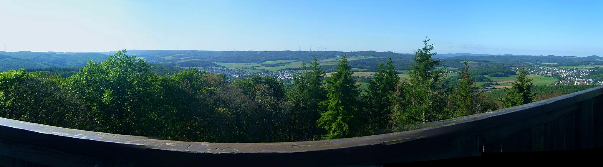 Photo showing: Blick vom Koppeturm im Höhenzug Zollbuche bei Erdhausen auf die Bottenhorner Hochflächen; rechts der Rimberg (498 m; 12 km entfernt), links davon die Kappe (494 m; 11,3 km); weiter links und eine Reihe dahinter Arennest (592 m; 19,4 km) und Sackpfeife (674 m; 23,6 km) nebst Hainpracht (631 m; 22,3 km), links davon wird der Buchholz (643 m; 25 km) von einem Weihnachtsbaum verdeckt; in der Zwischenreihe der Schwarzenberg (561 m; 17,3 km), dann die Hochflächen mit Allberg (528 m; 7 km) und Daubhaus (552 m; 6,7 km) rechts der Mitte und Angelburg (609 m; Sendeanlage) und Schmittgrund (590 m; unmittelbar rechts des Buchenzweigs) links der Mitte; im linken Hintergrund der westlichere Teil der Zollbuche. Zwischen Zollbuche und Hochflächen das Salzbödetal mit Bad Endbach, Wommelshausen (rechts davon und etwas höher), Weidenhausen (Mitte des Bildes), rechts oberhalb dann Römershausen und Rachelshausen (links vor dem Daubhaus); ganz rechts Gladenbach, links davon und durch den Lammerich (357 m) separiert, Kehlnbach. Siehe Udeuschle