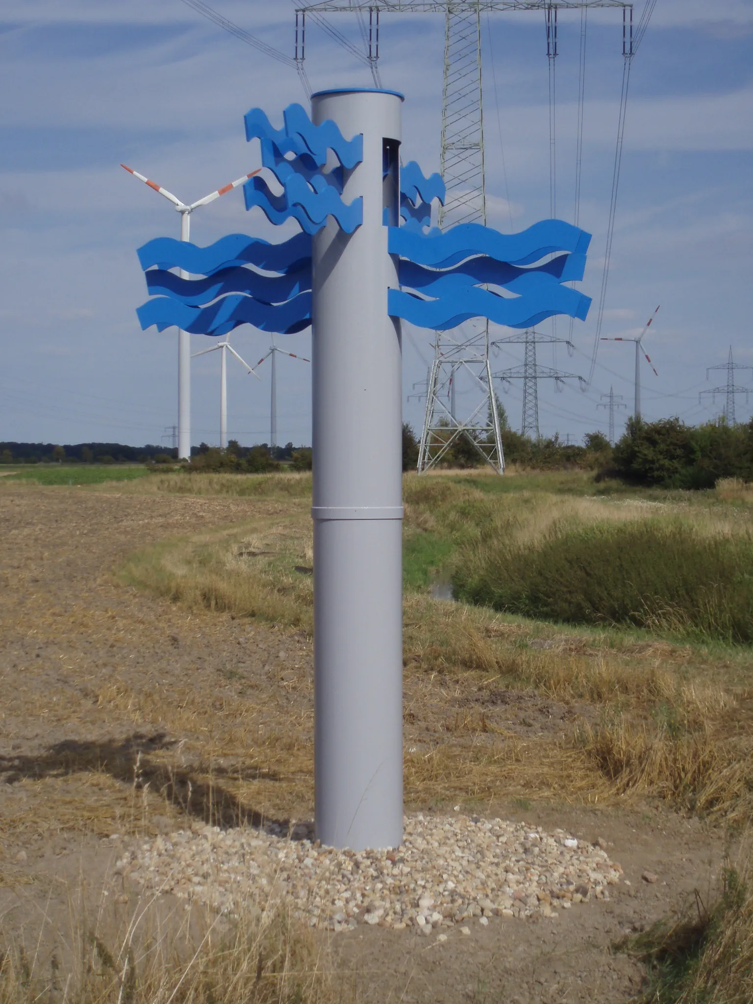 Photo showing: 65 m-Landmarke im Verlauf der Burgdorfer Aue; Skulpkur "Wasserwegekreuzung" von Reiner Hildebrandt in Sehnde-Dolgen; dahinter 380-kV-Freileitung und WKA